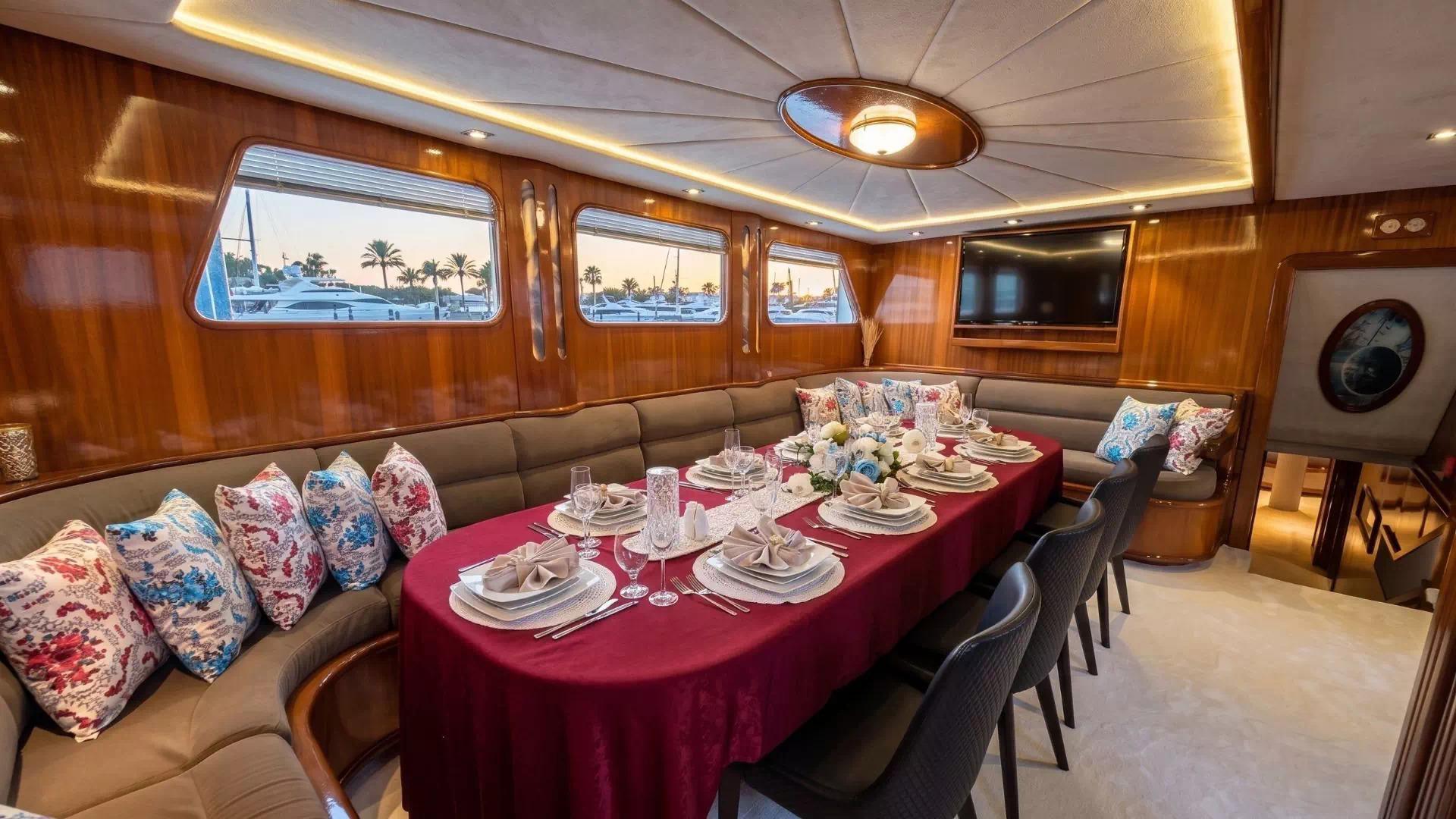 yacht dining saloon with burgundy tablecloth, place settings, built-in seating and portholes
