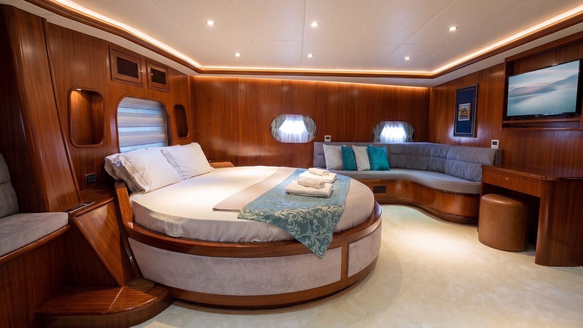 luxury yacht master cabin featuring circular bed, curved sofa seating, oval portholes and warm wood paneling