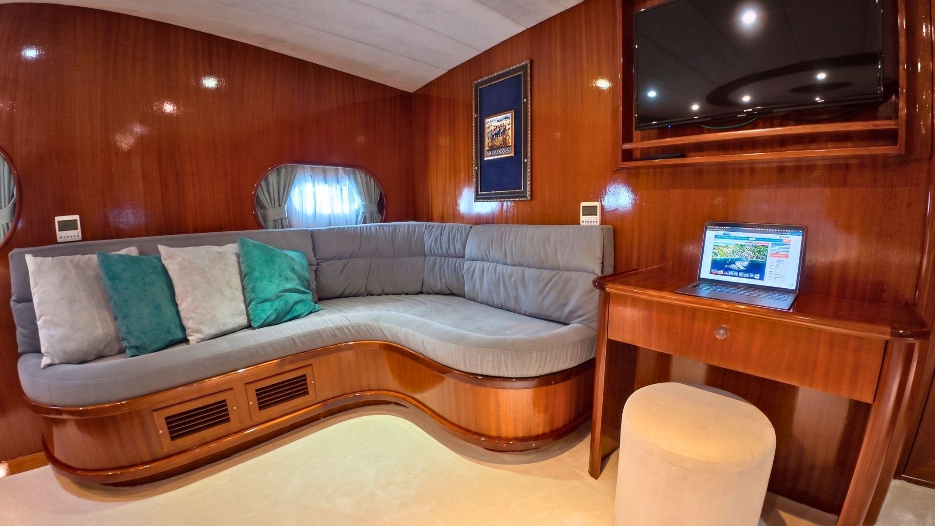 yacht salon interior with curved grey seating, wood paneling, and integrated desk with laptop