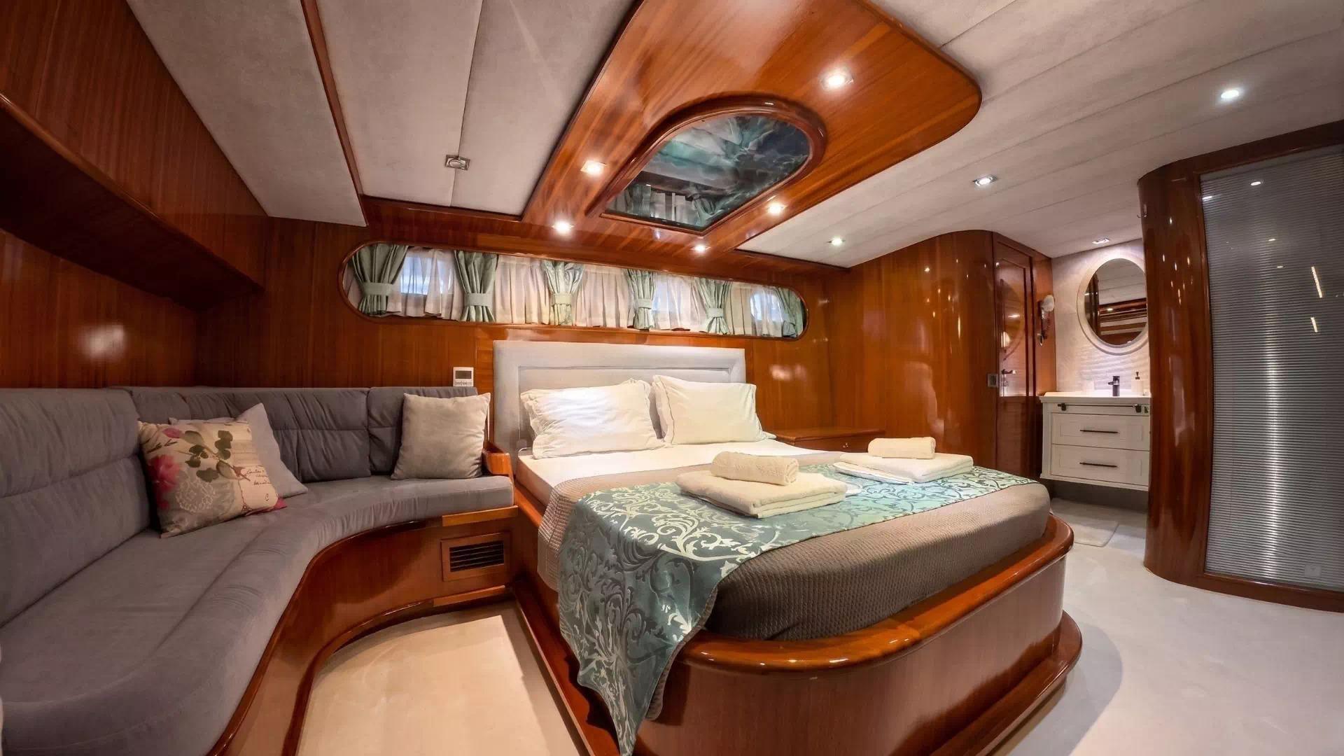luxury yacht master cabin featuring double bed with white linens, grey sofa seating, and en-suite bathroom