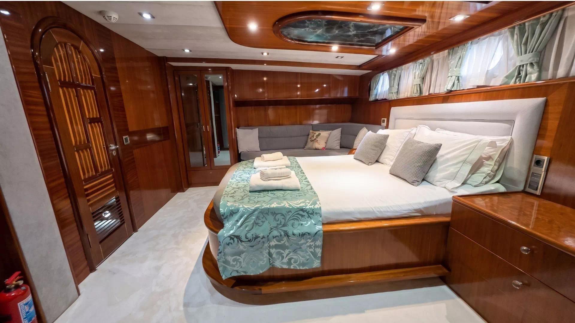 Master cabin interior featuring king bed with turquoise runner, built-in seating and rich wood paneling