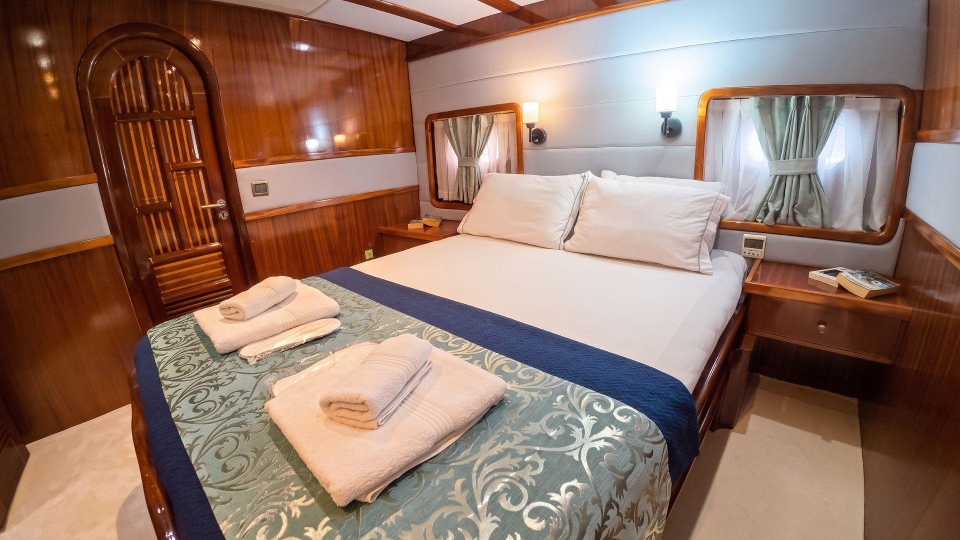 yacht guest cabin featuring double bed with blue runner, wooden paneling and twin portholes