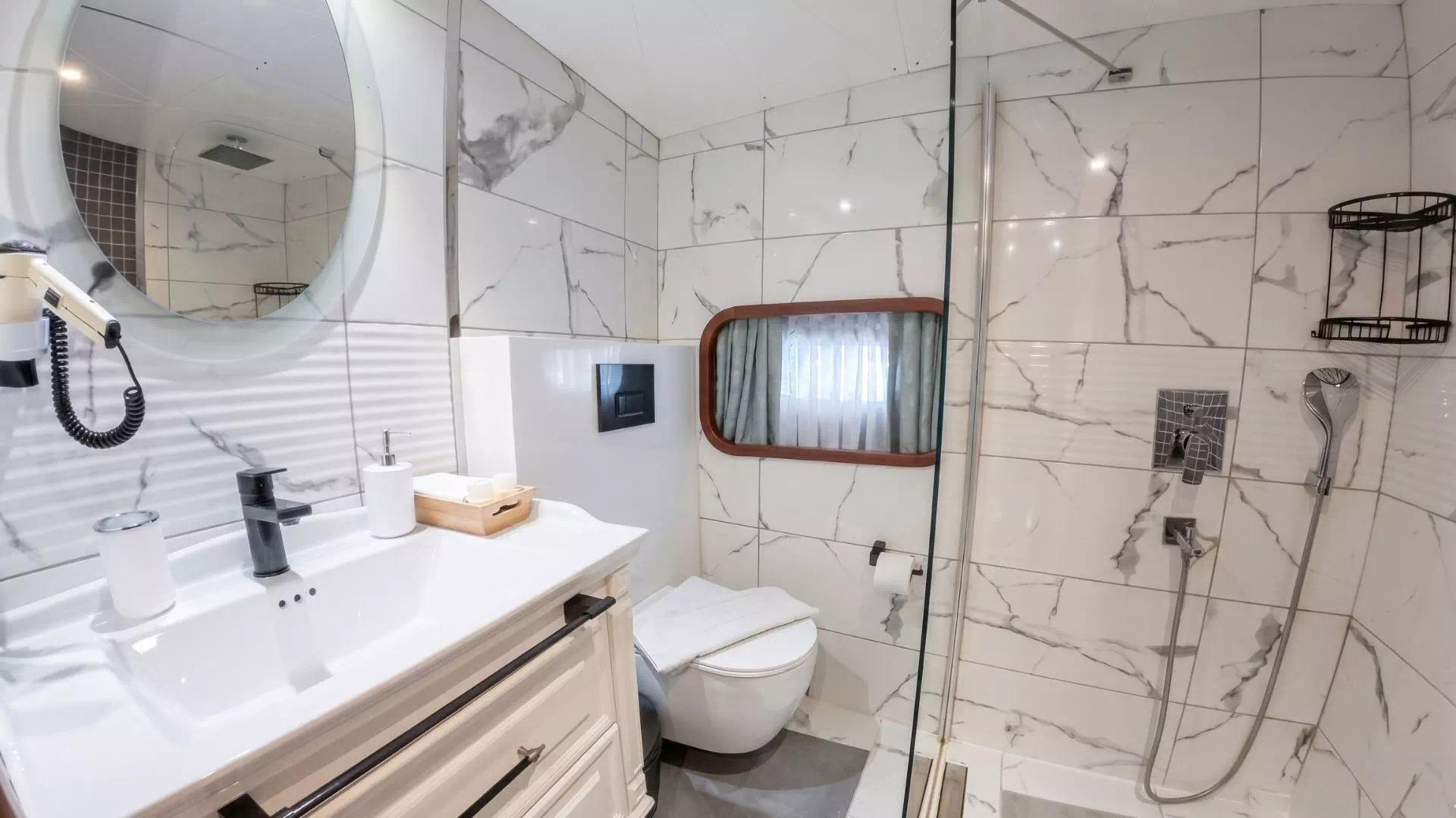 luxury yacht bathroom featuring white marble walls, glass shower enclosure, vanity with mirror and porthole window