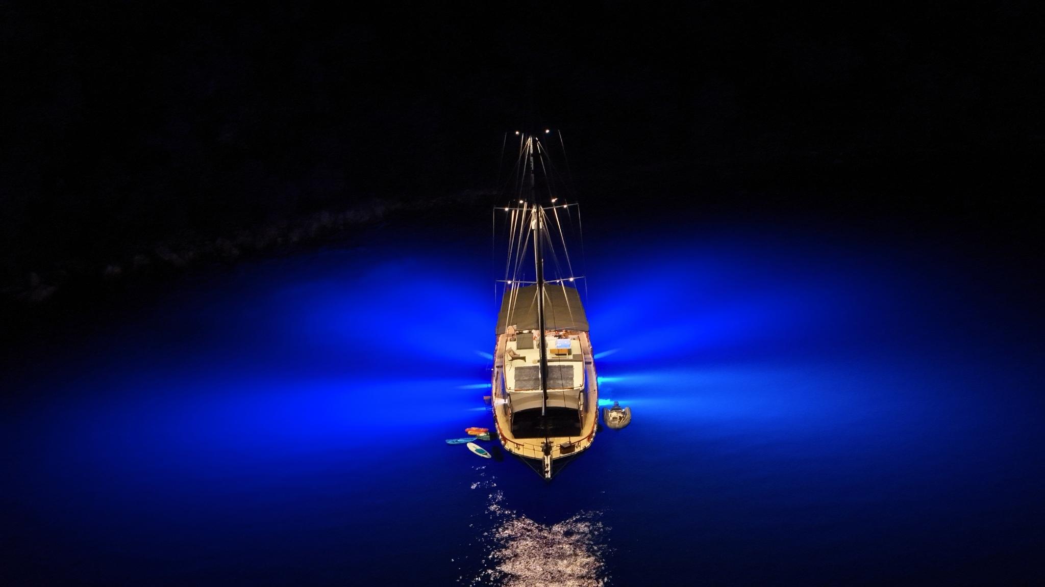 aerial night drone shot of gulet yacht glowing with blue underwater lights at anchor