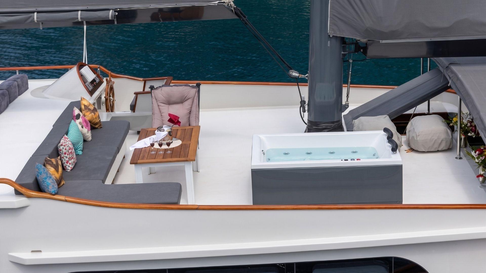 gulet sun deck jacuzzi with water jets, grey L-shaped sofa, teak coffee table and traditional wooden helm wheel