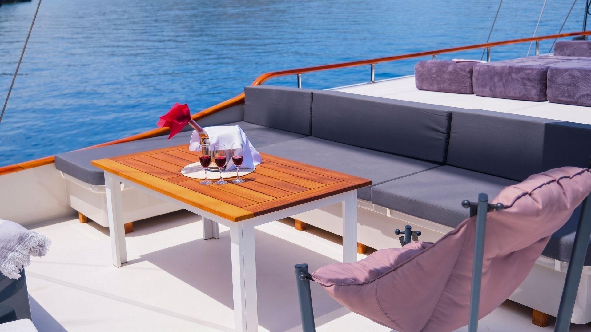 Three glasses of red wine and chilled bottle on teak coffee table on gulet aft deck