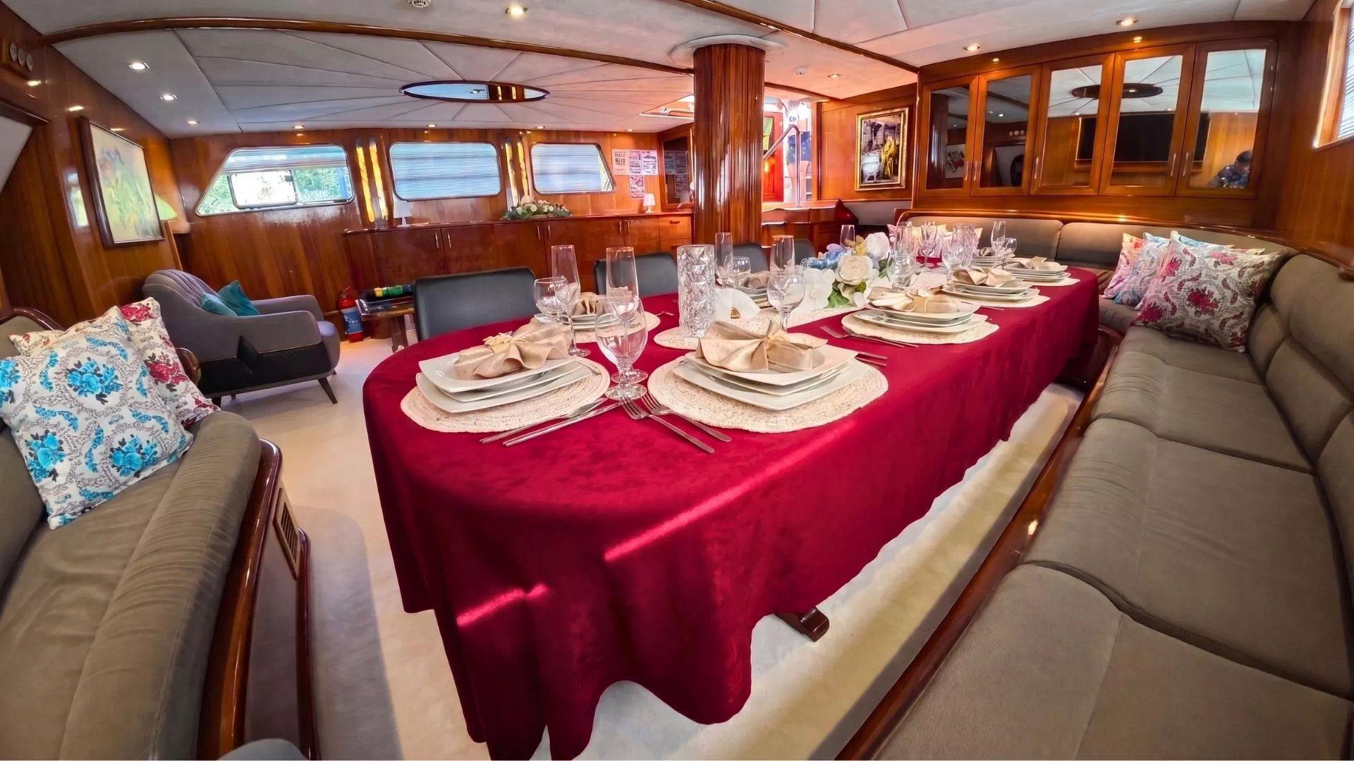Gulet salon dining table covered in red velvet cloth set with crystal glasses, white china plates, and folded linen napkins for ten guests