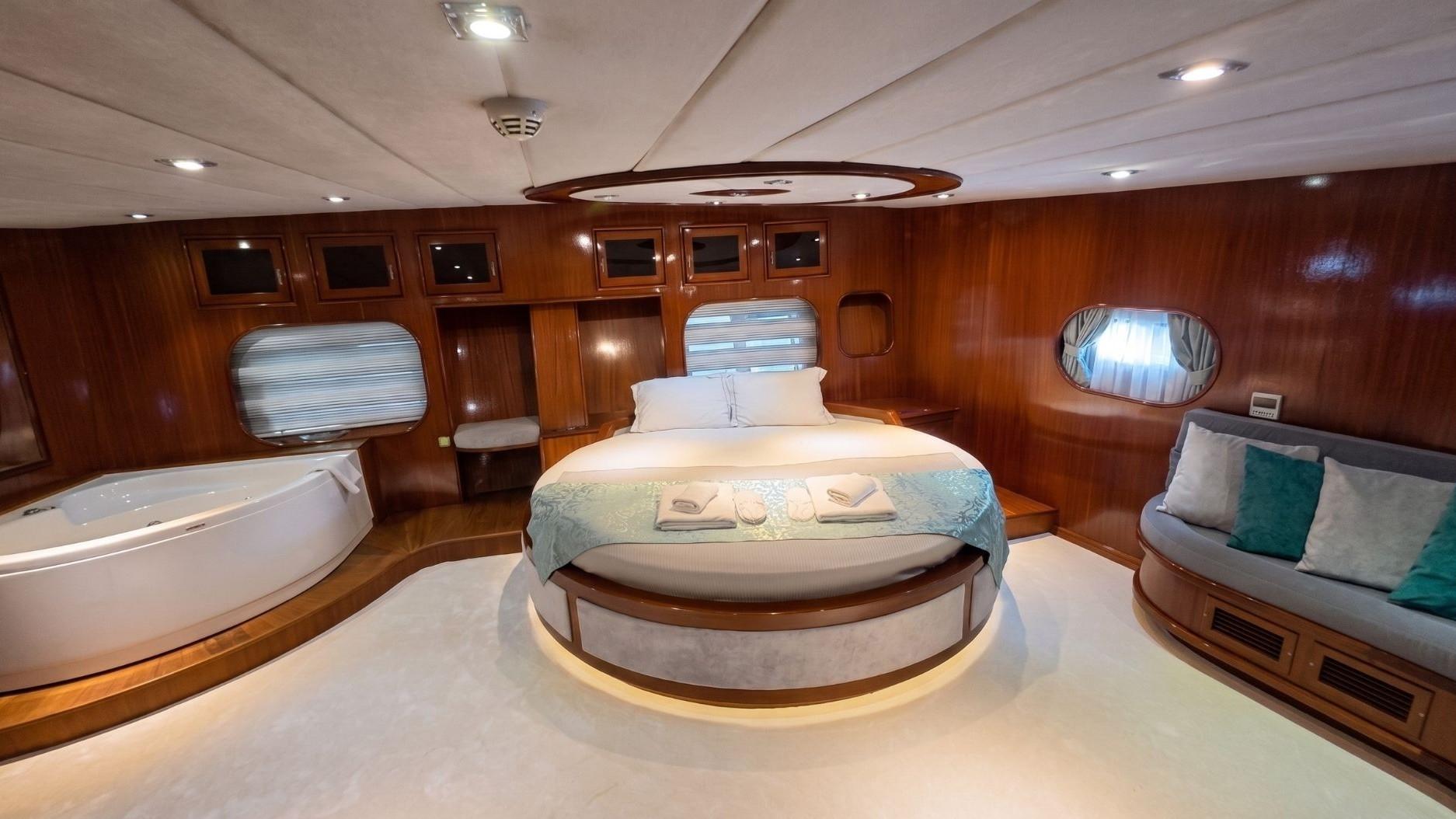 luxury master cabin featuring circular king bed with under-lighting, in-cabin white jacuzzi tub, and teak wood panelling