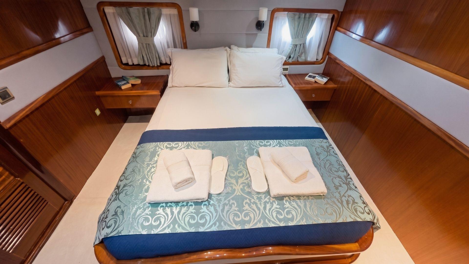 Gulet double cabin with king bed, blue damask runner, folded towels, guest slippers, and walnut panelling