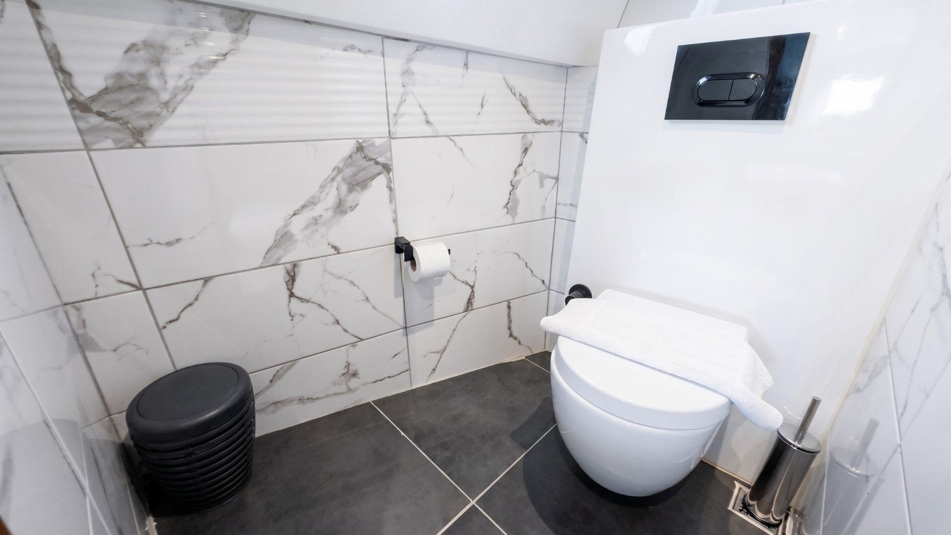 Yacht en-suite bathroom with large-format marble wall tiles, wall-hung white toilet, black flush plate, and dark floor tiles