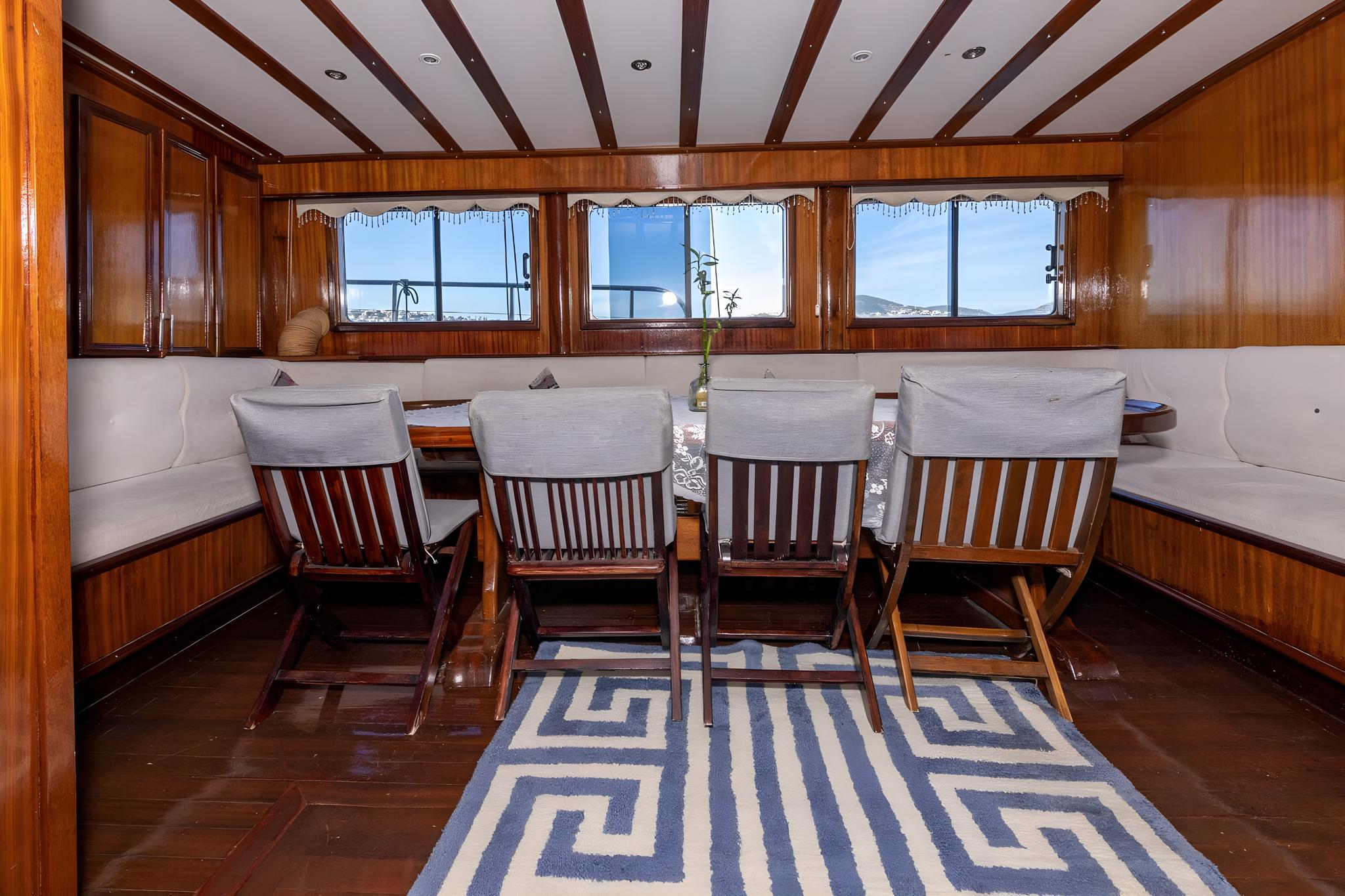 yacht interior dining saloon with wooden table, cushioned seating and panoramic windows
