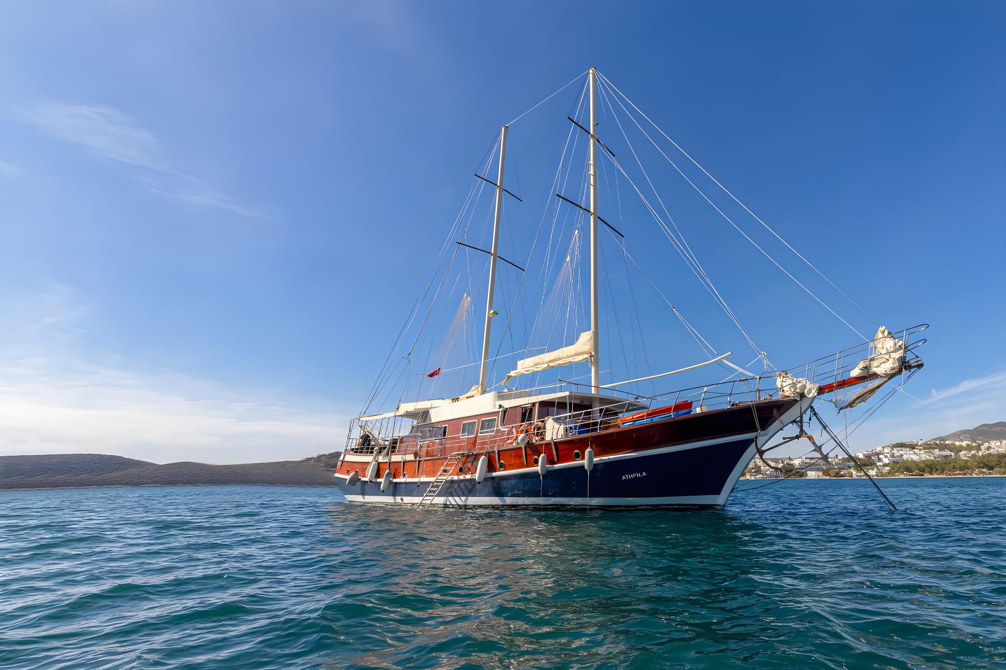wooden gulet yacht with two masts anchored in clear turquoise waters near Mediterranean coastline