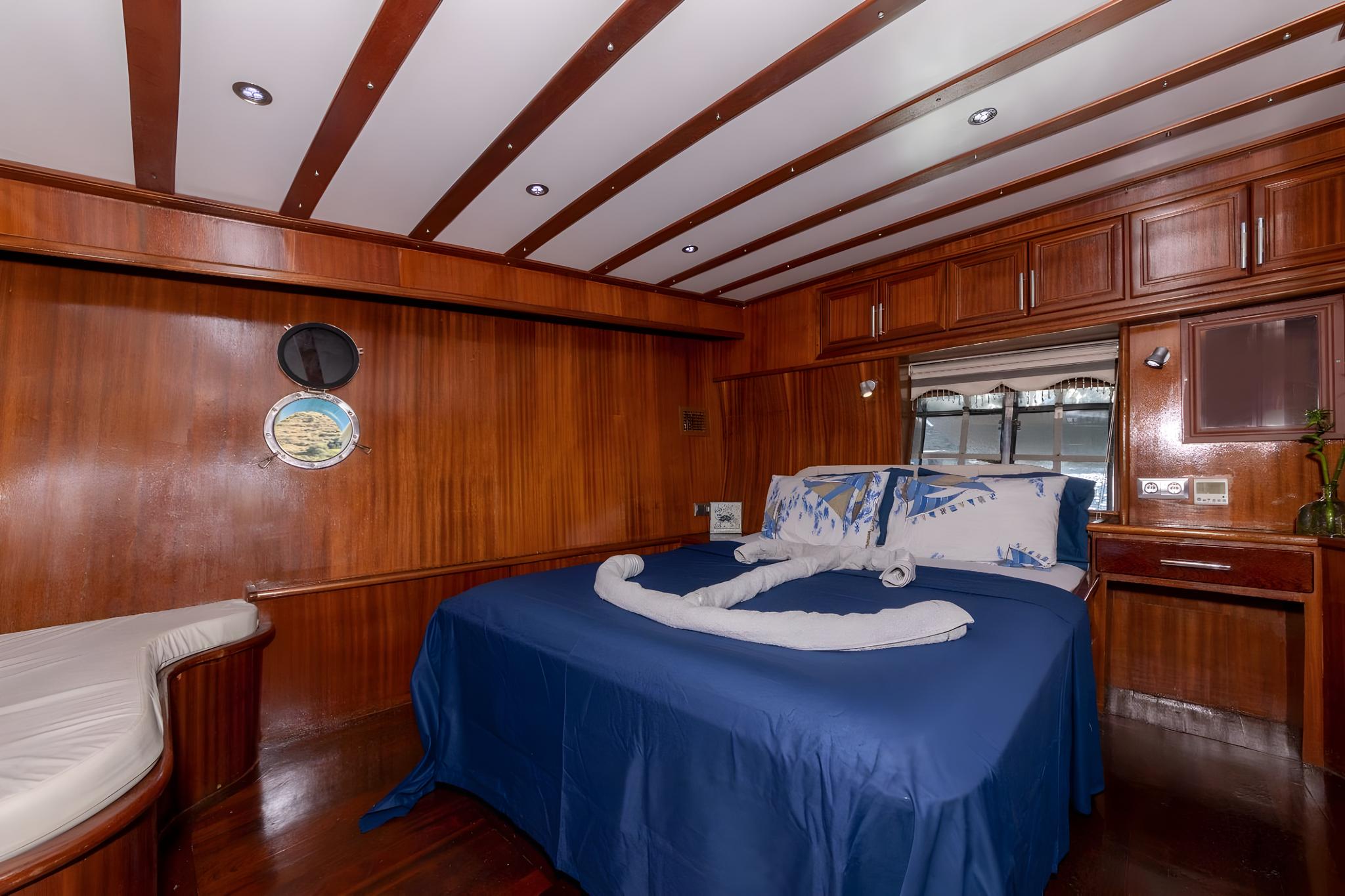 luxury yacht master cabin featuring king bed with blue bedding and mahogany wood interior
