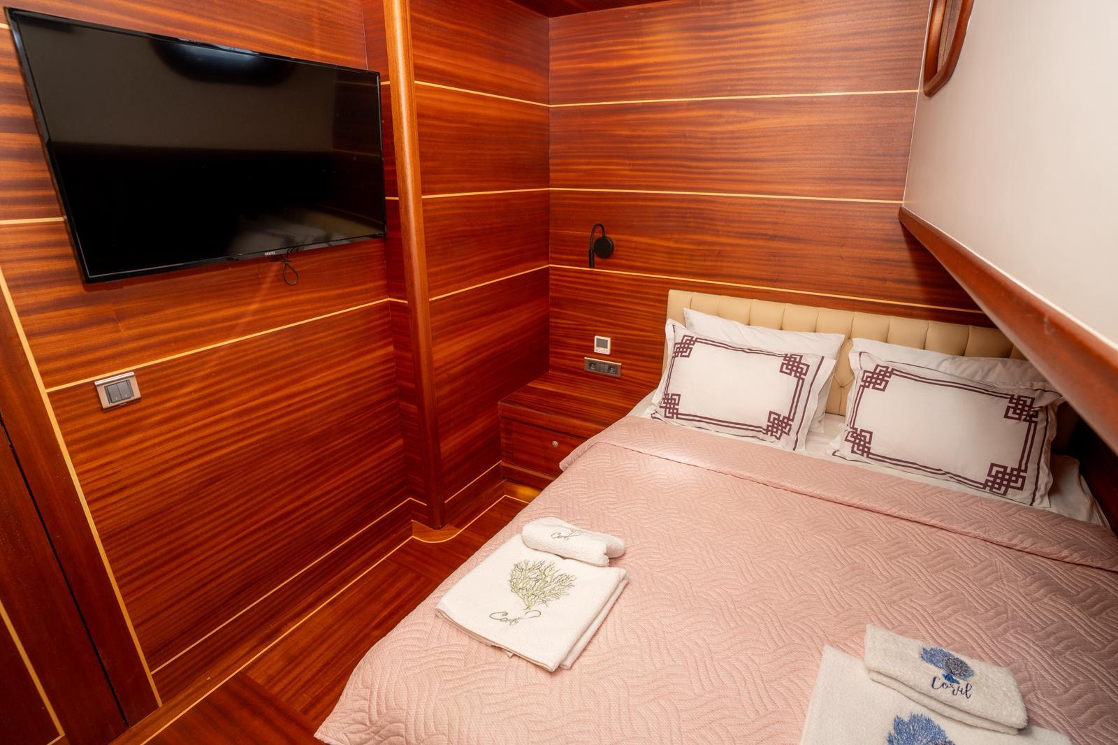 yacht cabin interior with double bed, wood paneling, wall-mounted television and white linens