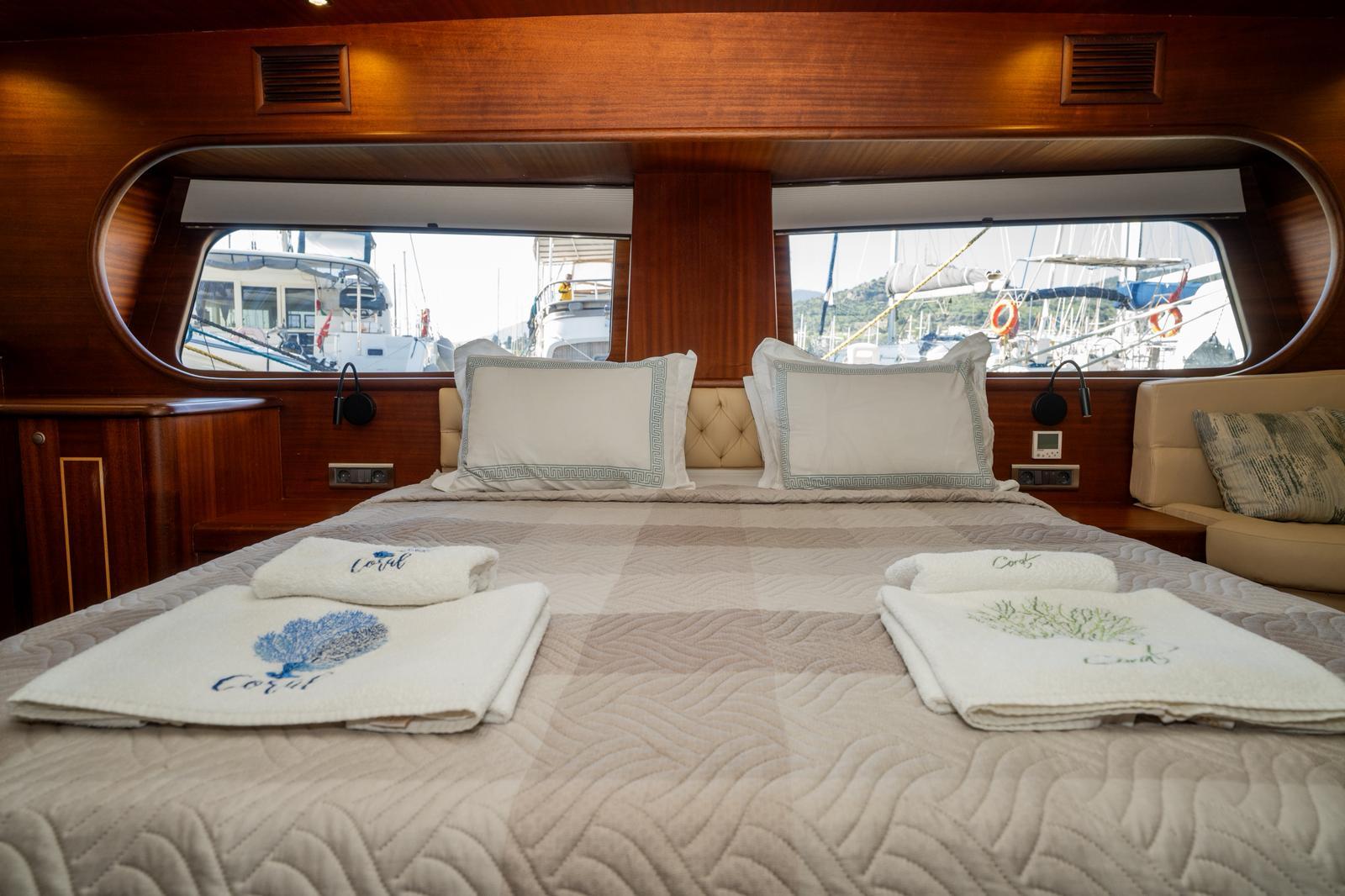 yacht cabin interior with quilted double bed, pillows, towels and large panoramic windows showing marina