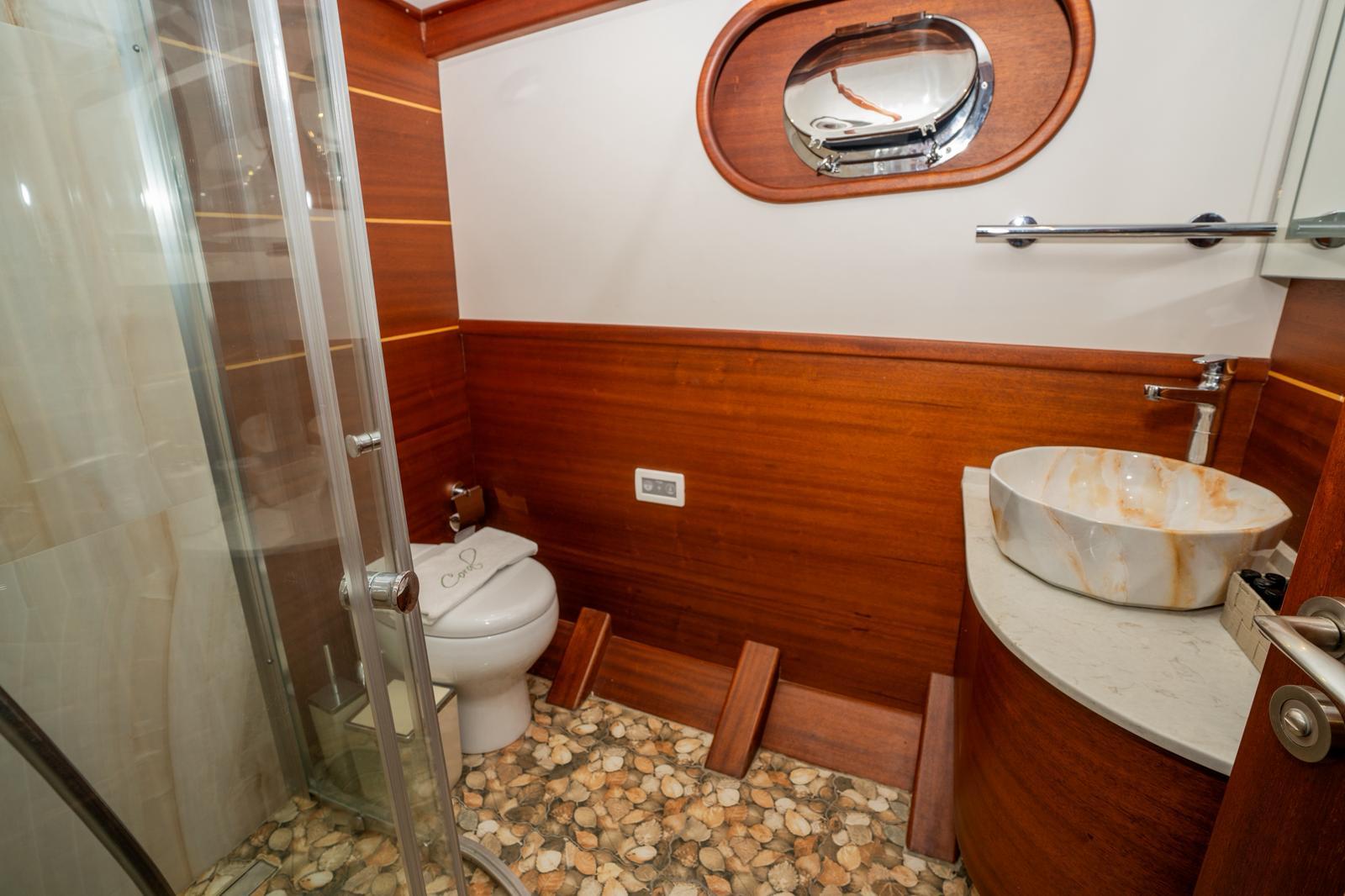 yacht ensuite bathroom featuring glass shower, toilet, marble vessel sink and rich wood paneling