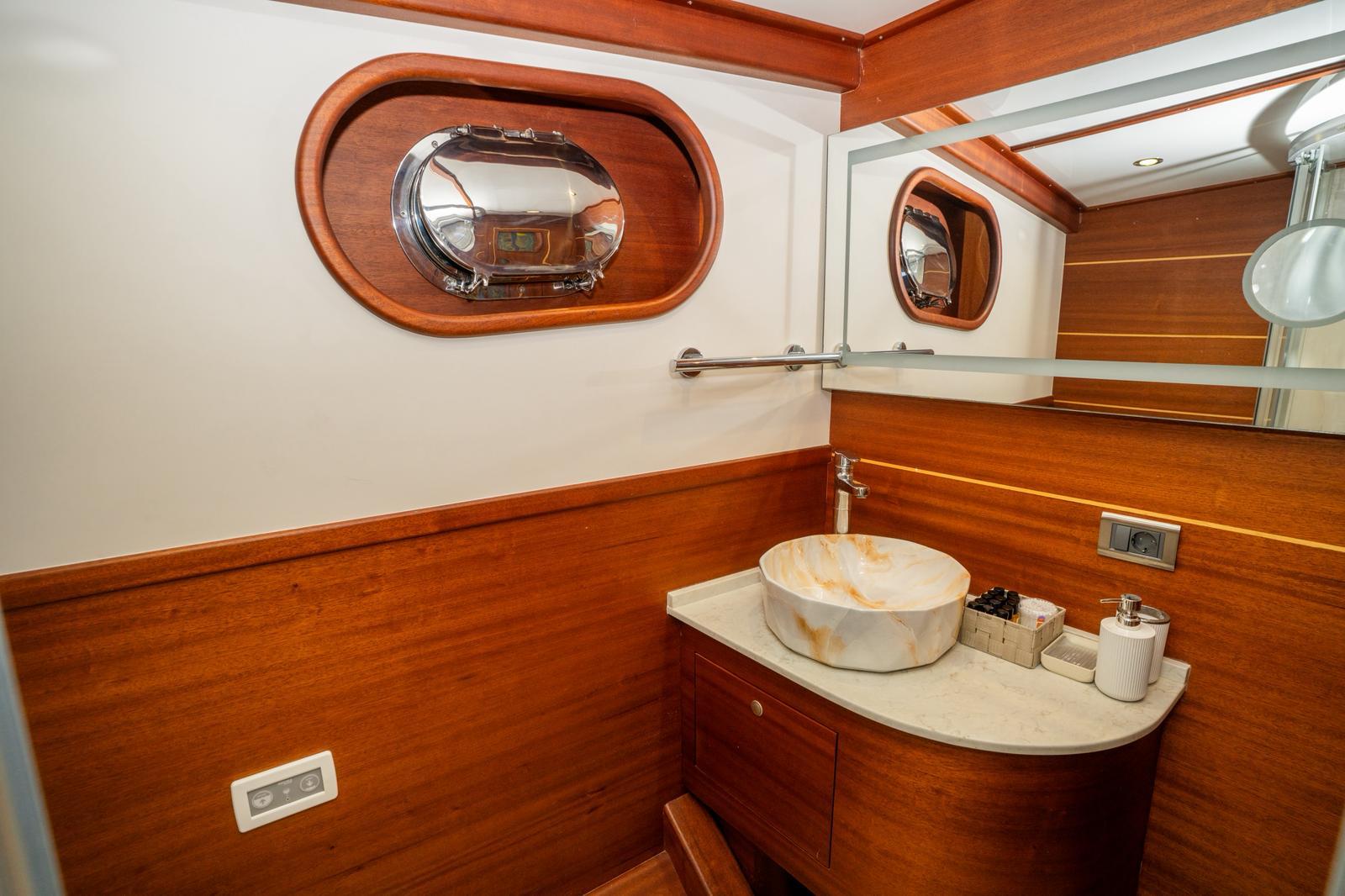 luxury yacht bathroom featuring marble vessel sink, teak paneling, and oval porthole window