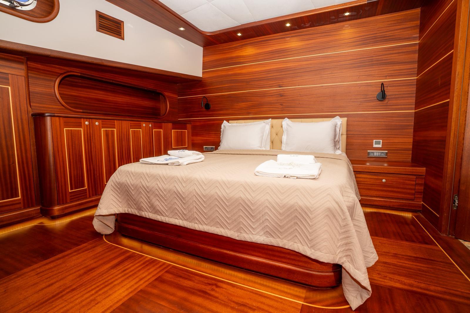 Master cabin interior with king bed, rich wood paneling, built-in wardrobes and white linens