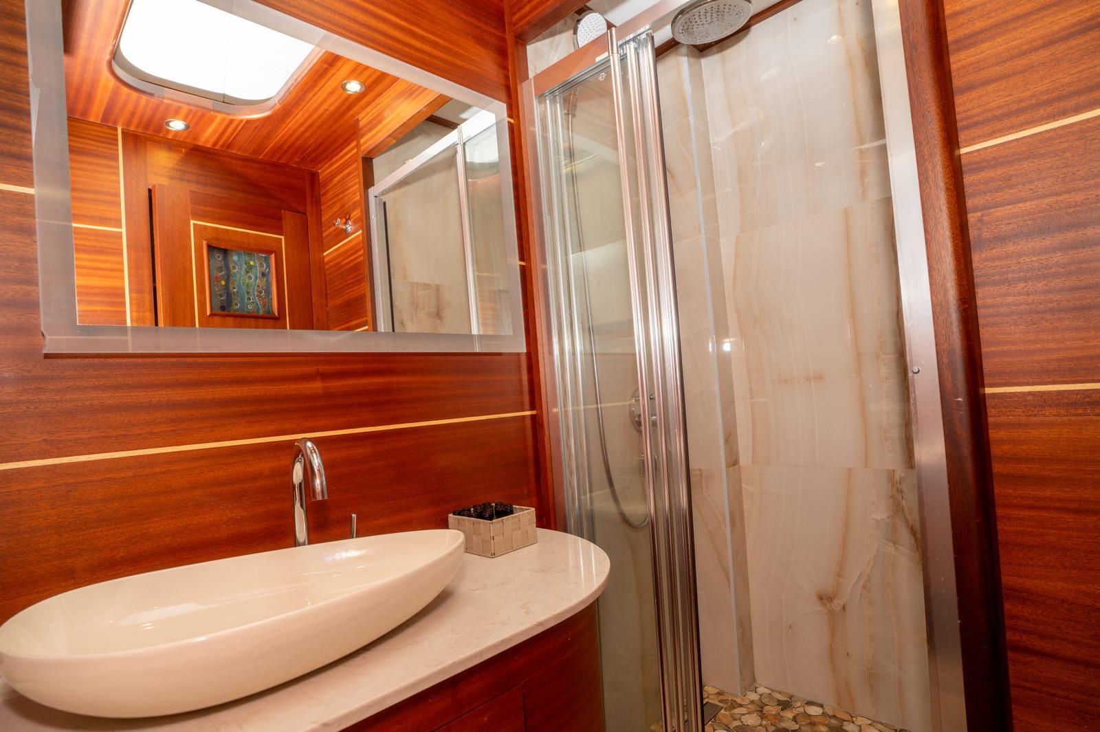 yacht bathroom featuring white basin sink, large mirror and glass shower cubicle