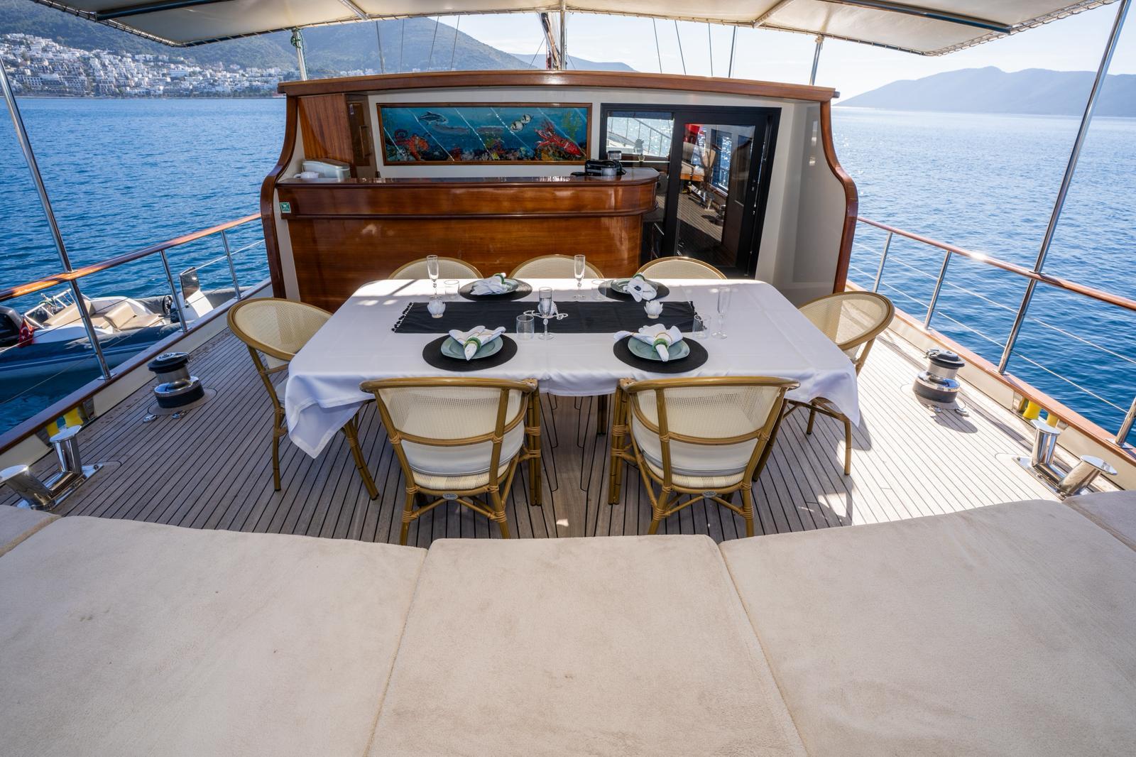 Aft deck dining table with white tablecloth and formal place settings under awning