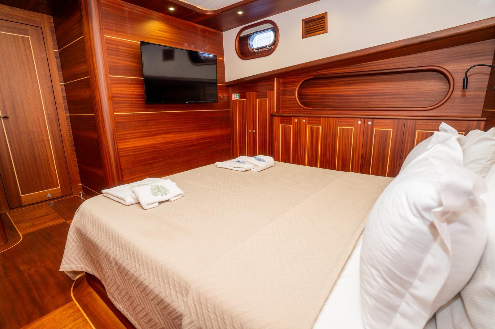 yacht guest cabin with beige bedding, rich wood paneling, and flat-screen television