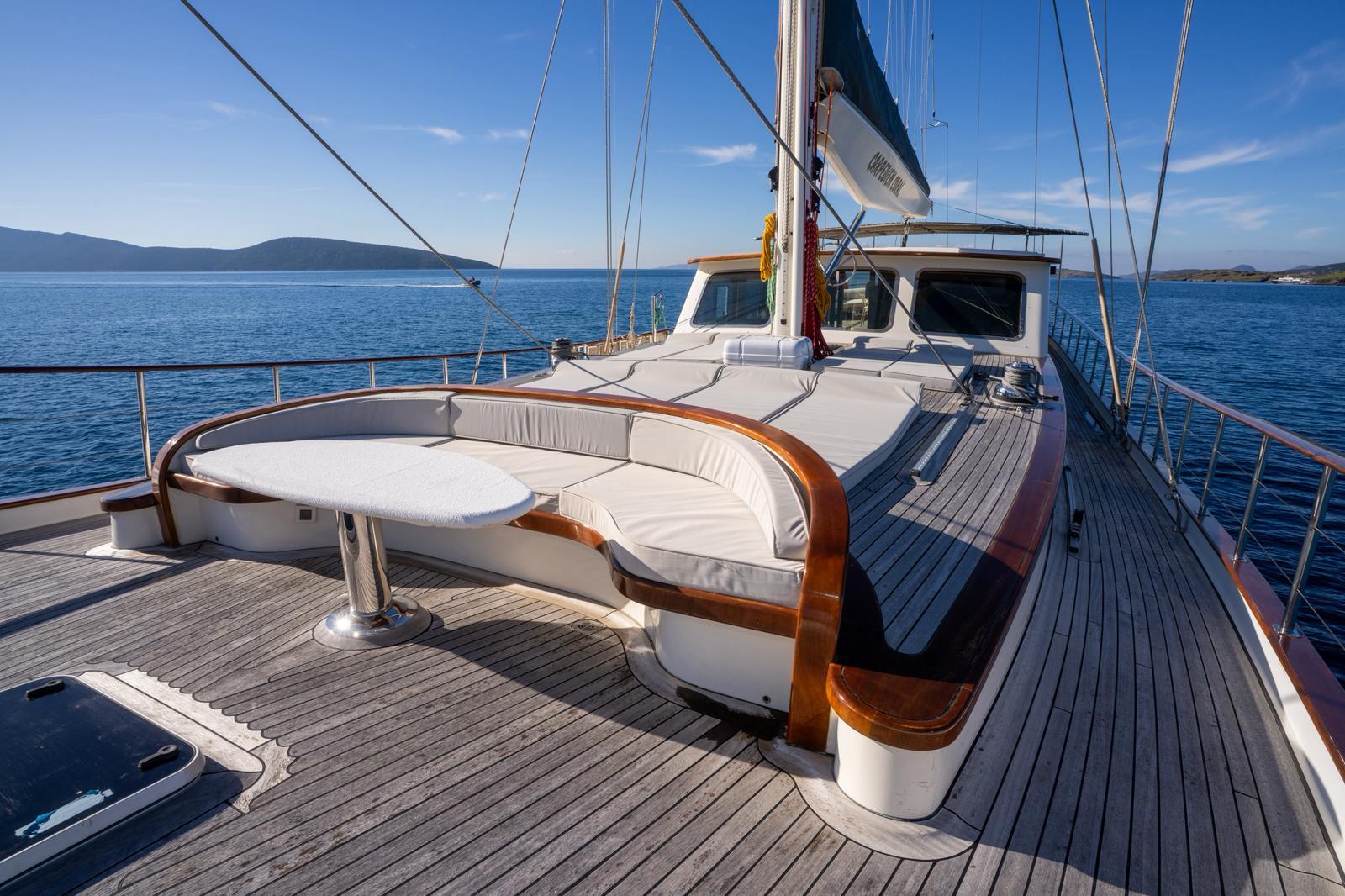 bow deck curved seating area with white cushions and teak decking on sailing yacht