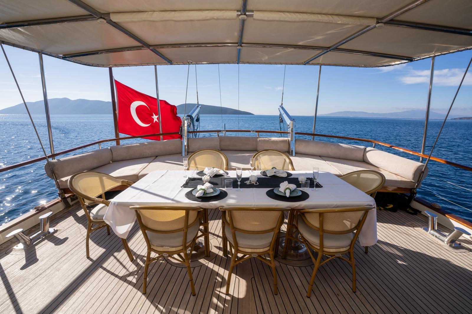 Yacht aft deck dining area with white table, wicker chairs and Turkish flag