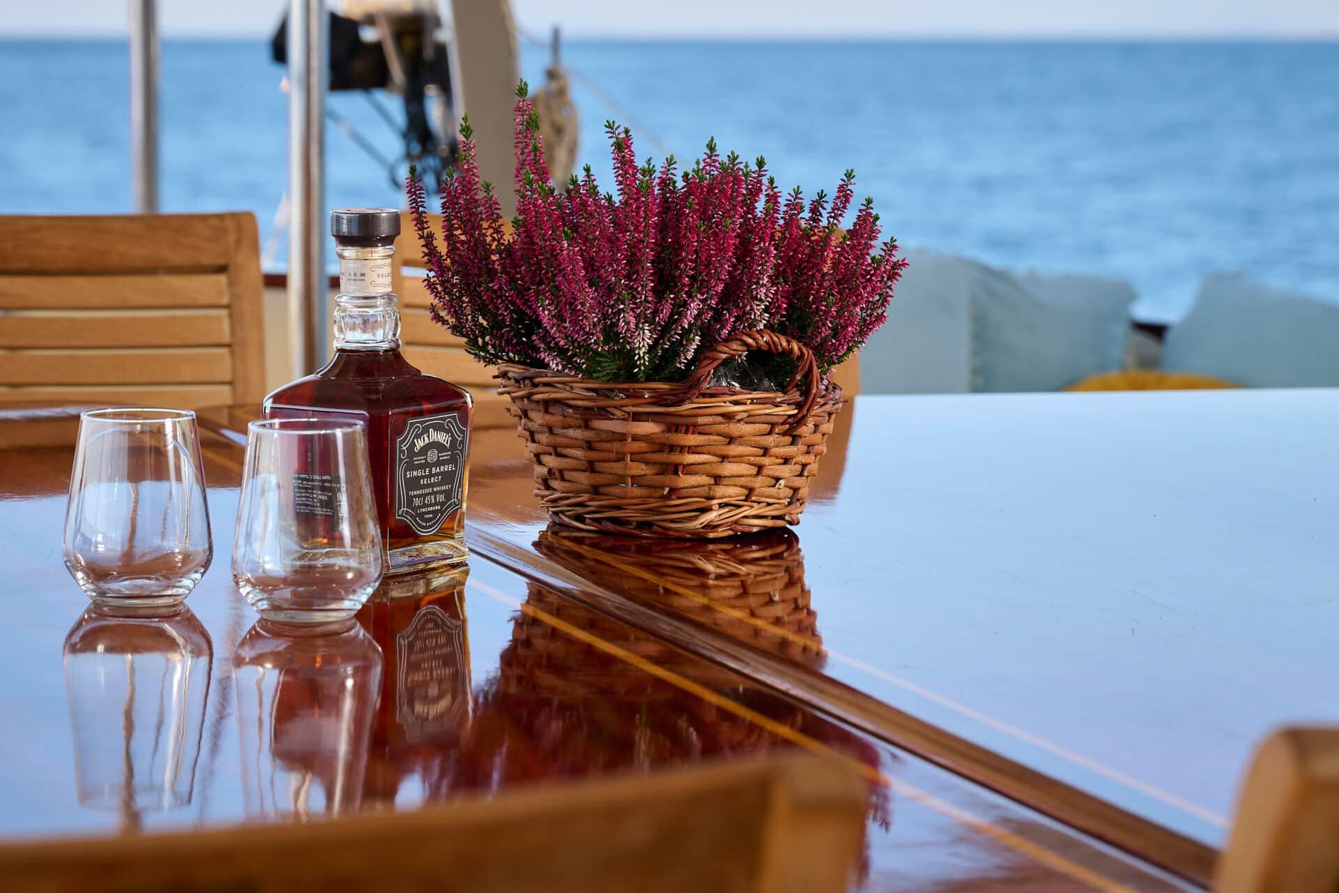 Jack Daniels whiskey bottle with two glasses on yacht dining table with purple flowers