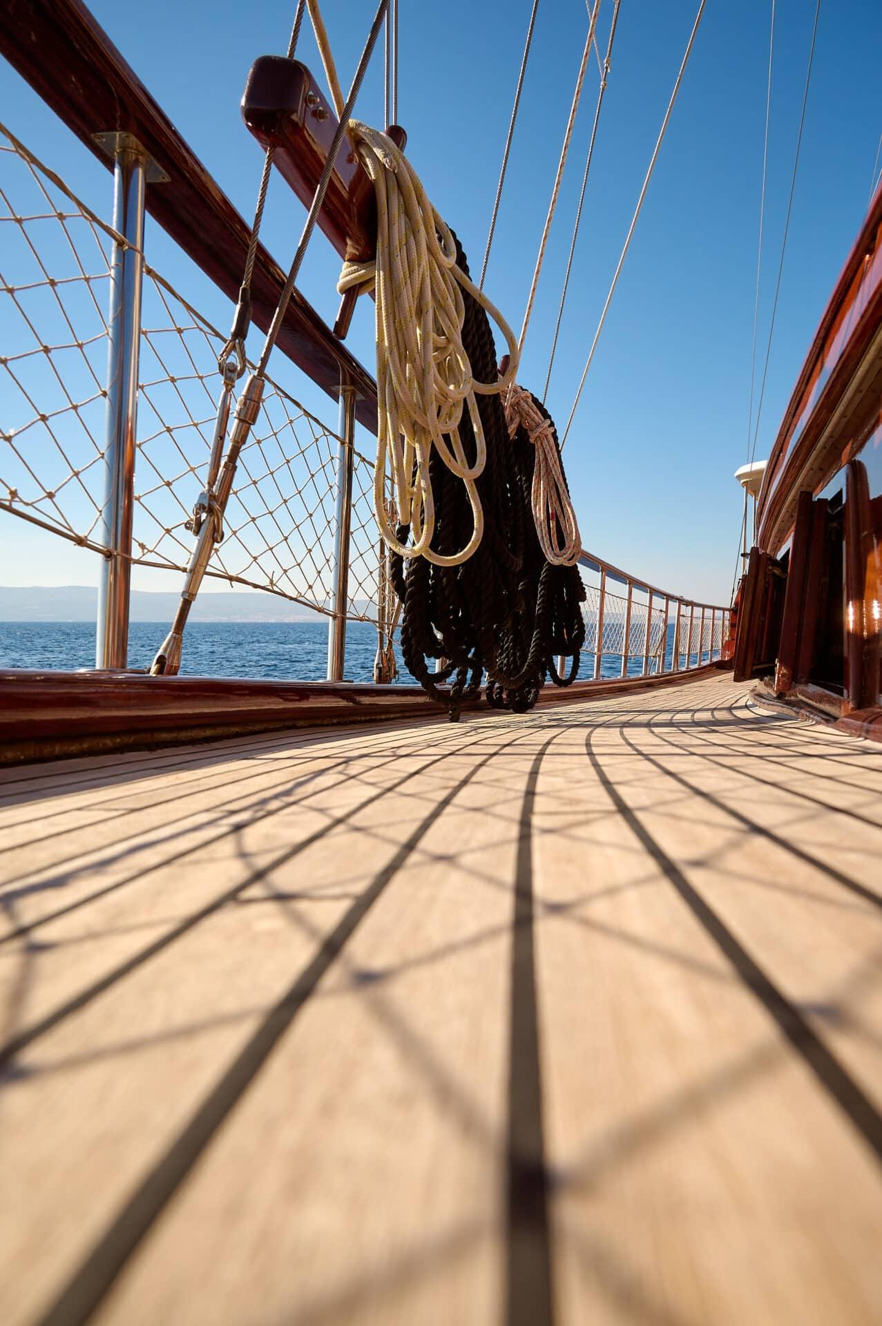 wooden deck of traditional sailing yacht with mast rigging and rope netting against blue sky