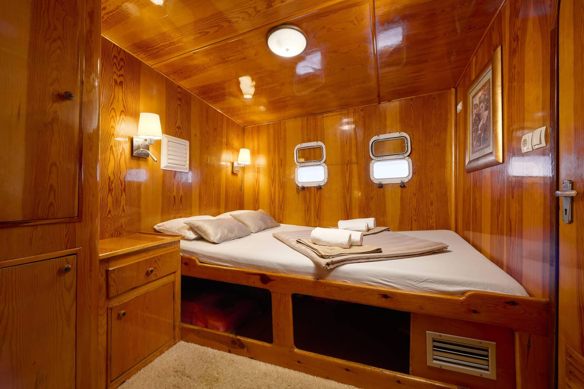 yacht guest cabin featuring double bed with white linens, built-in storage drawers, and two portholes