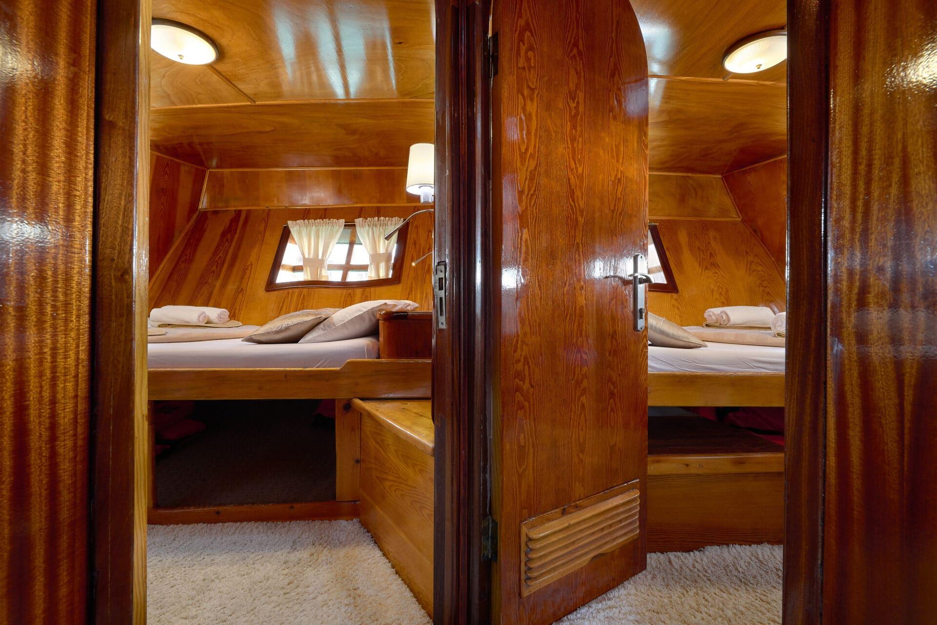 yacht guest cabin featuring wooden bunk beds with white linens and small portholes with curtains