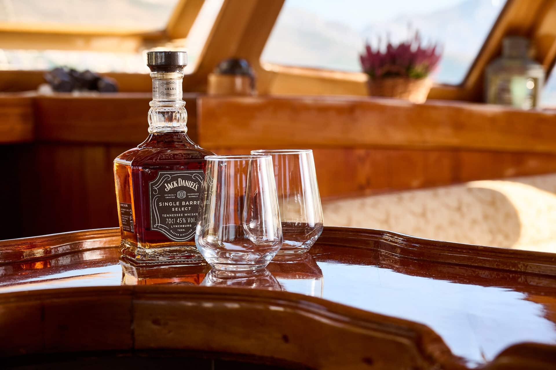 Jack Daniels Single Barrel Select whiskey bottle with two empty glasses on polished yacht salon table