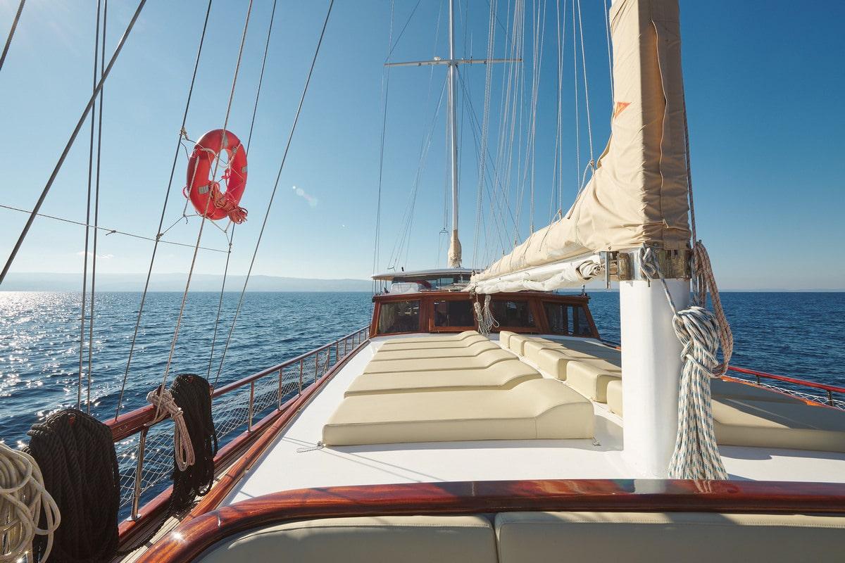 gulet forward deck with cream cushioned seating area, white mast and rigging visible