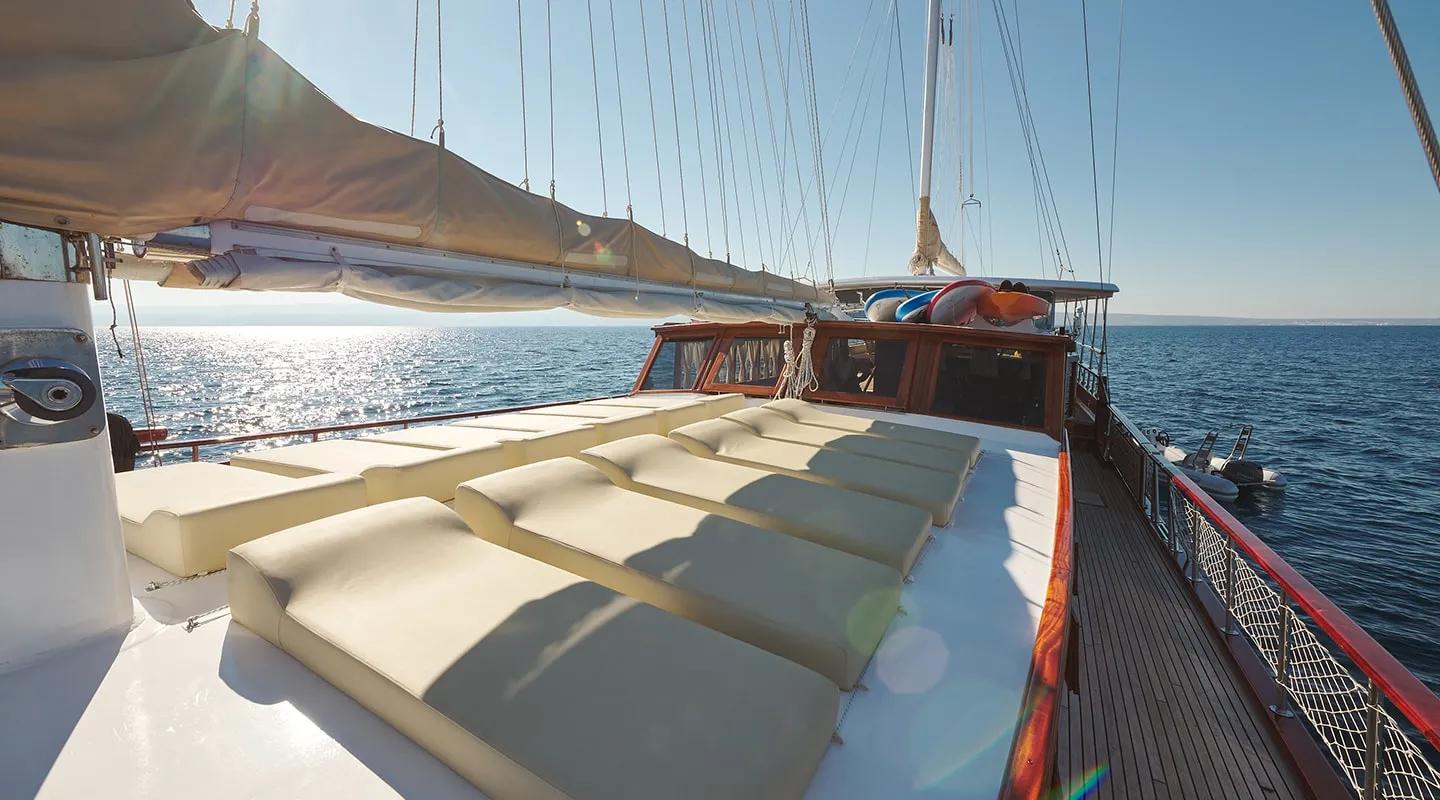 gulet bow deck with cream cushioned sun loungers and furled sails at sea