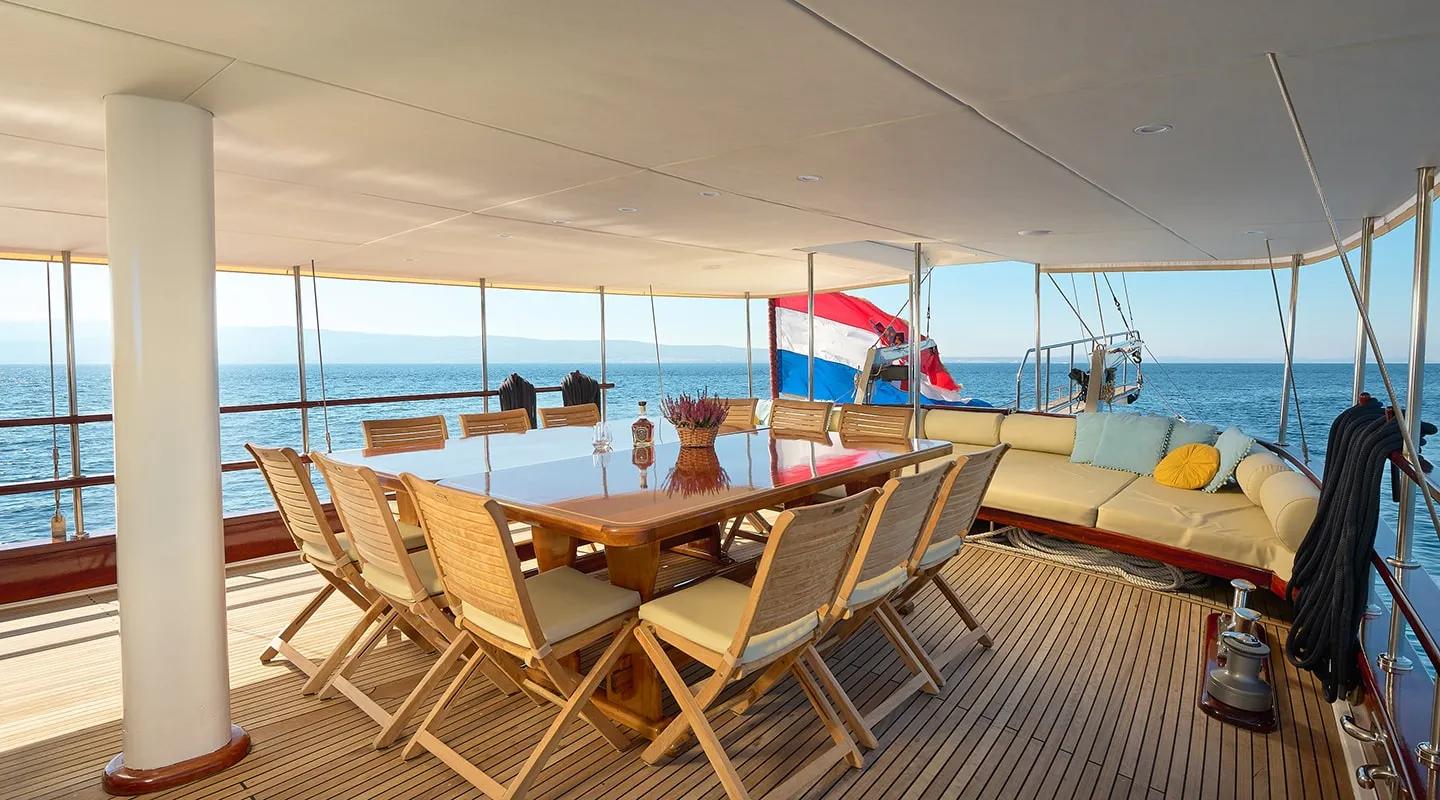 covered aft deck with teak dining table, folding chairs and built-in seating