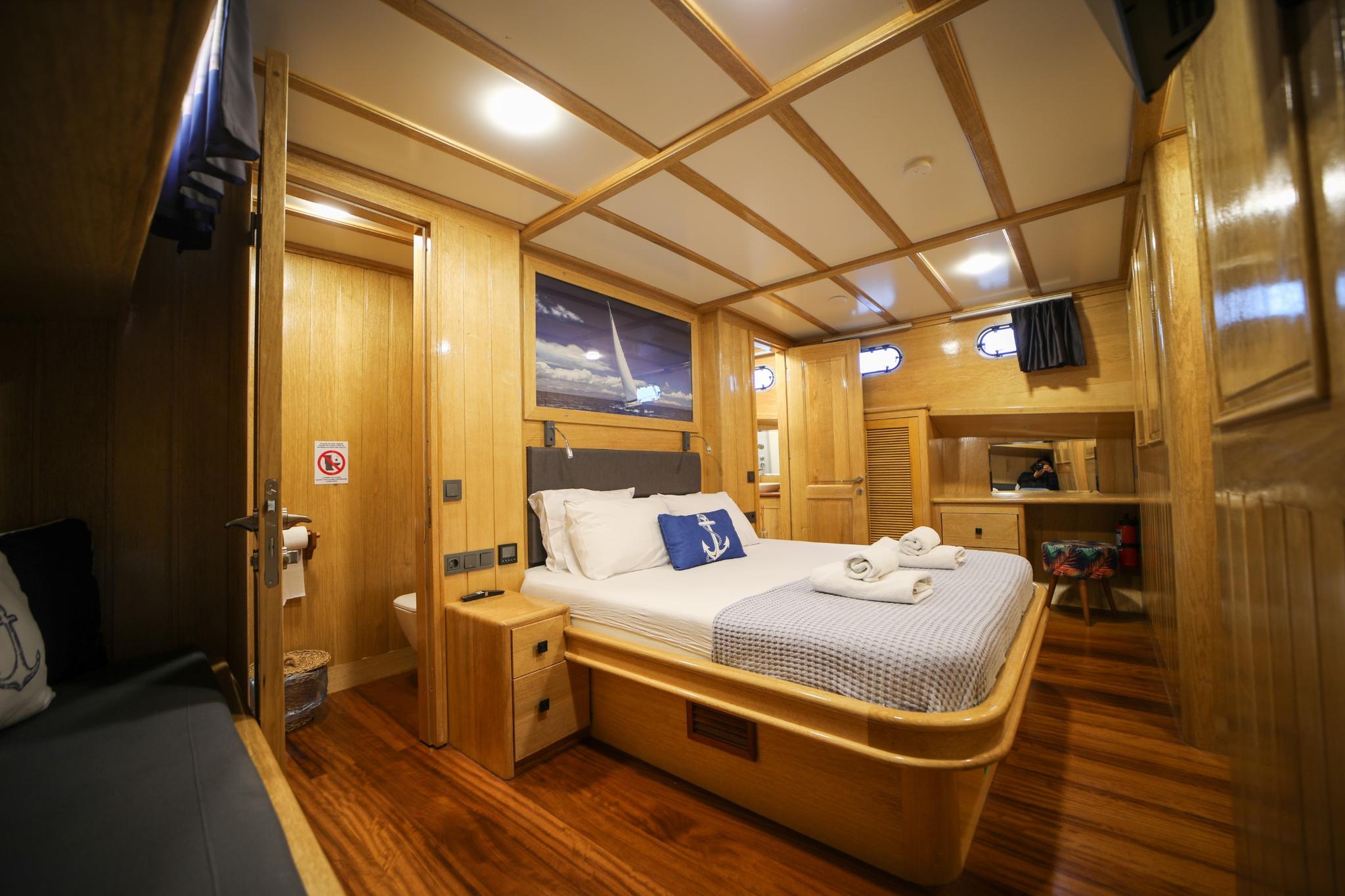 yacht guest cabin featuring double bed with white linens, blue anchor pillow, wood paneling and portholes