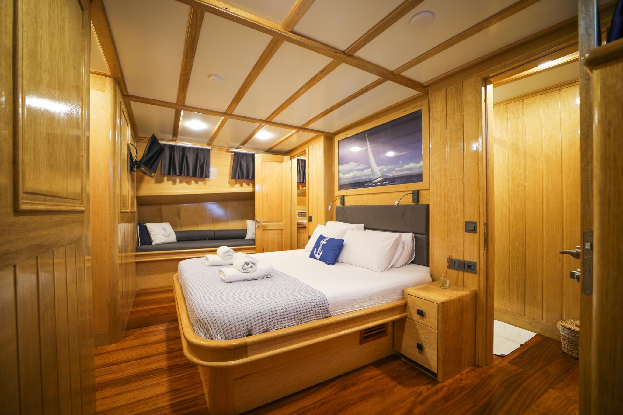 yacht guest cabin featuring double bed with white linens, built-in seating bench, and wood paneling