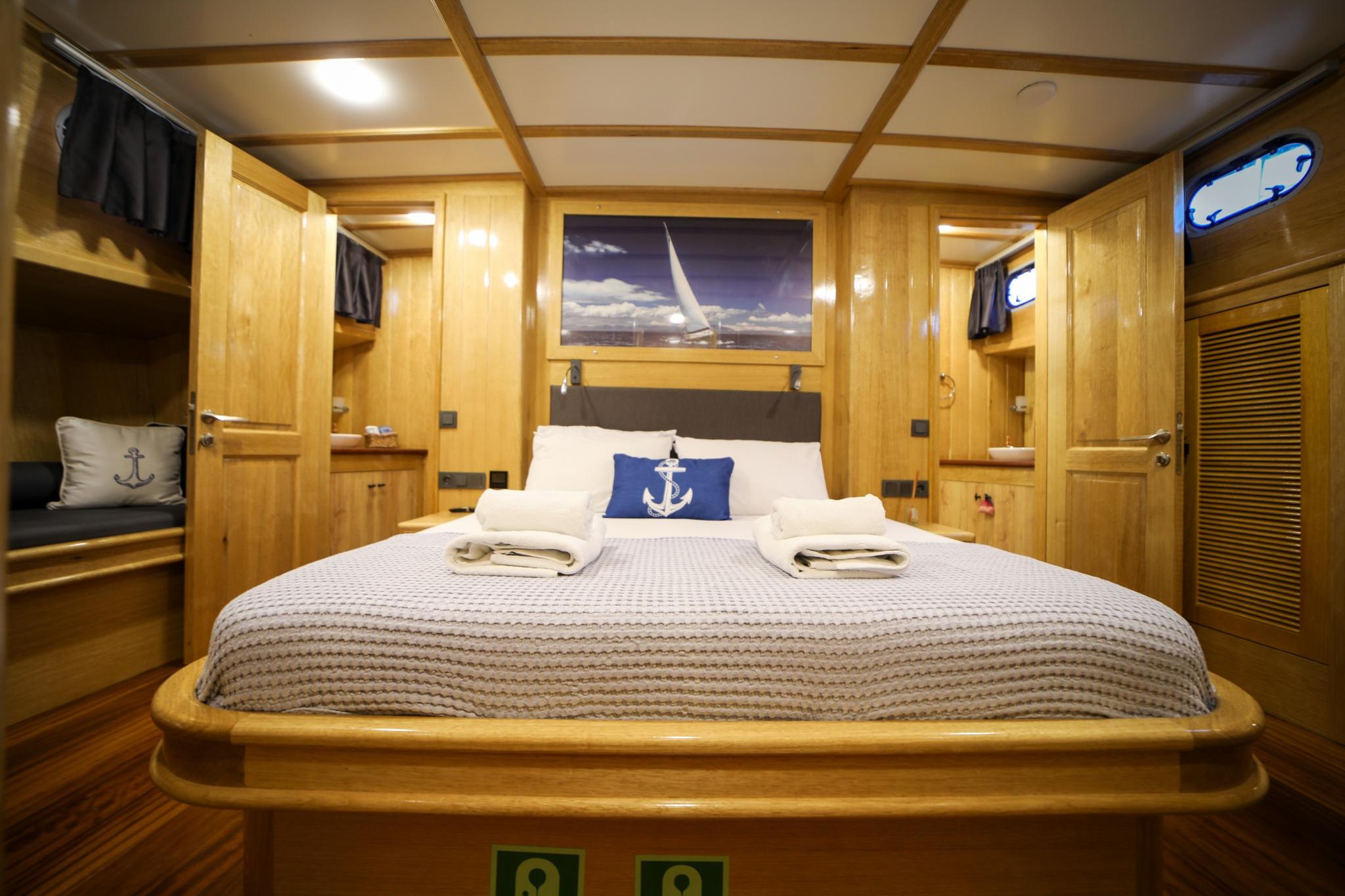 Master cabin with king bed, light wood paneling, nautical artwork and anchor pillows