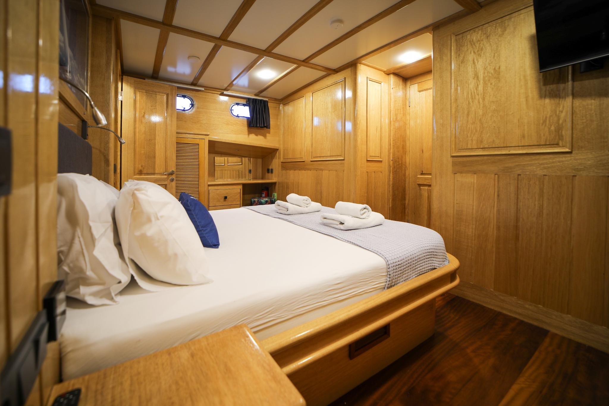 yacht guest cabin with double bed, wooden paneling, portholes and built-in wardrobes