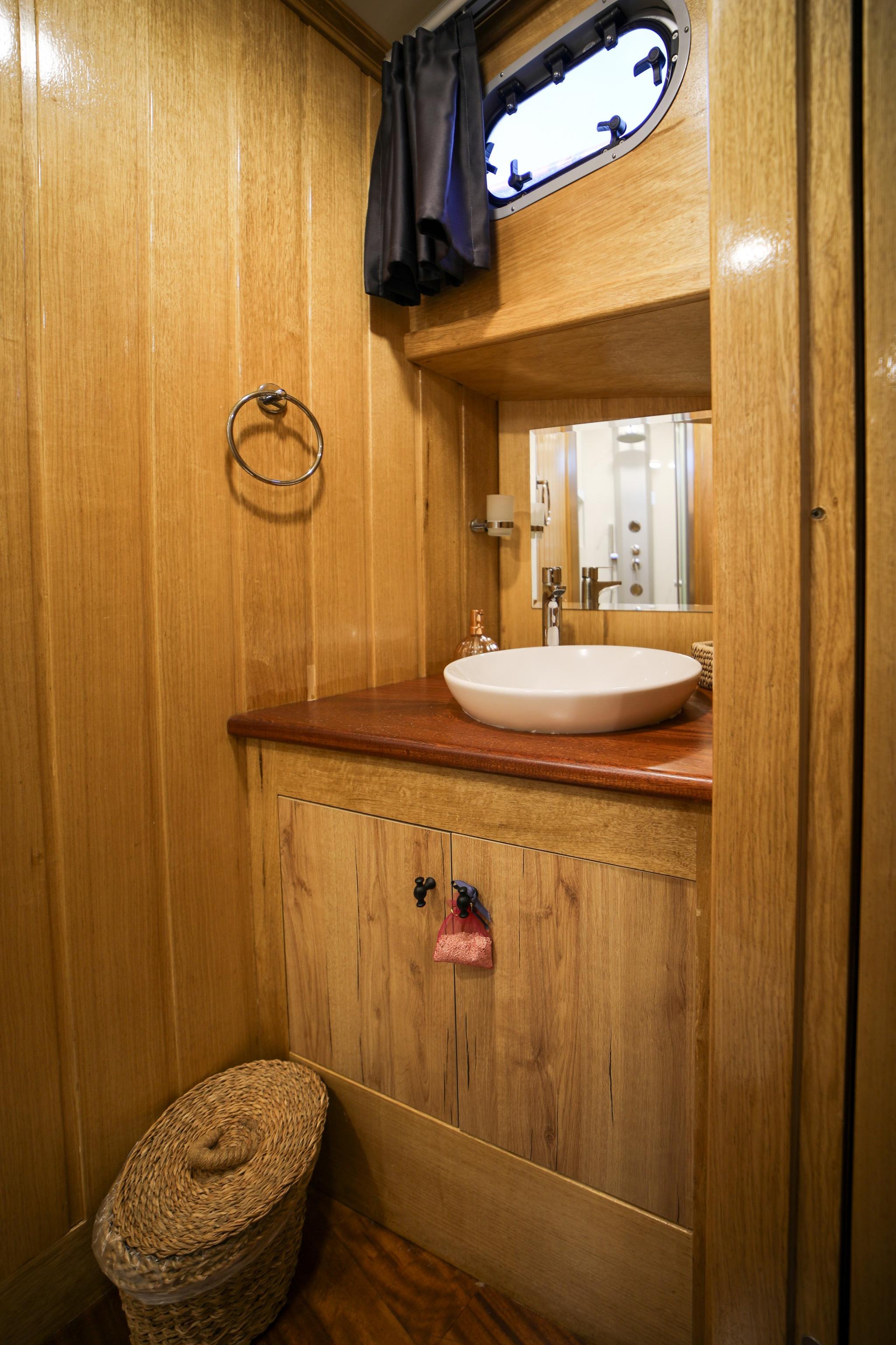 Yacht bathroom with white vessel sink on wood countertop and oval porthole window