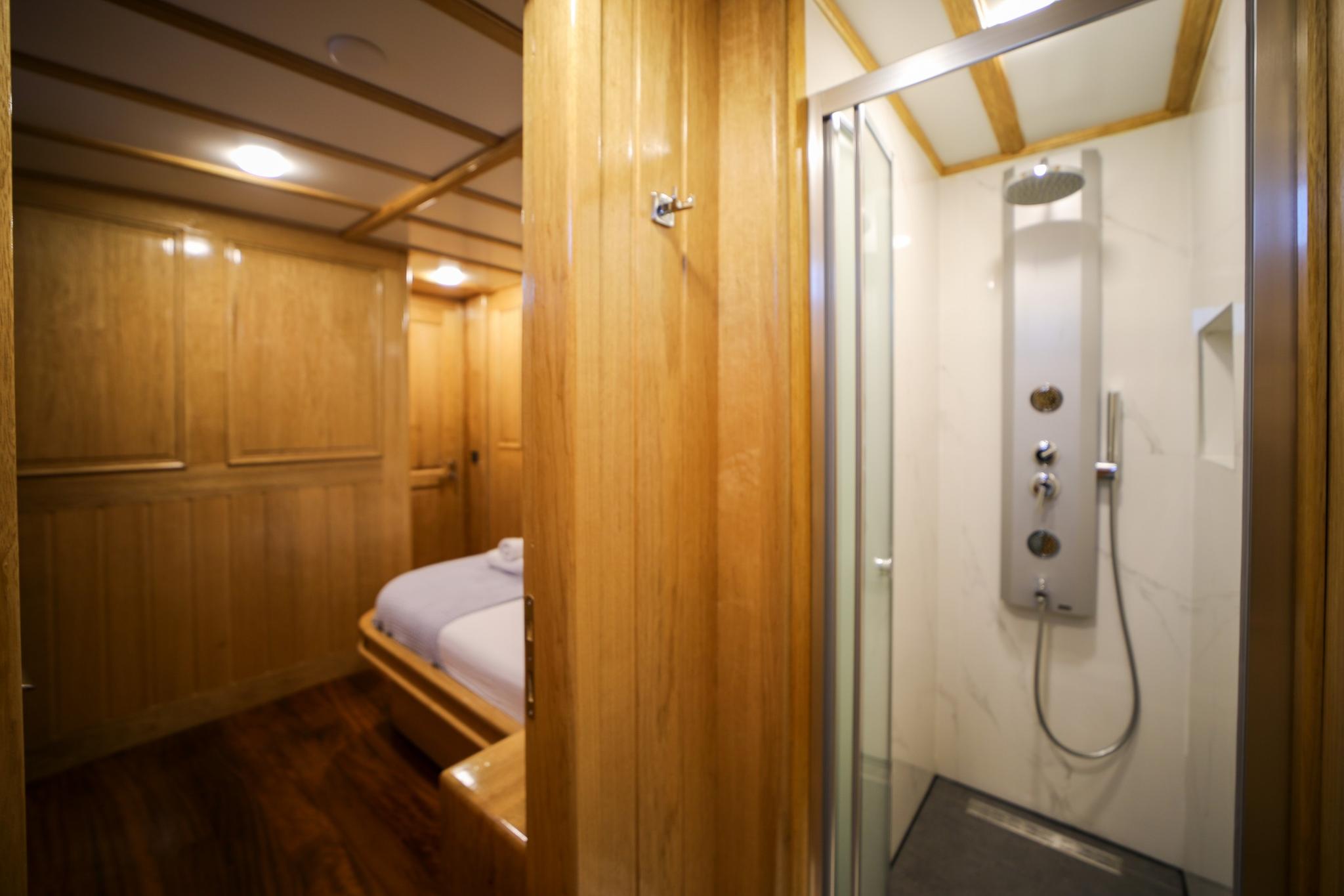 yacht guest cabin featuring single bed with white linens and adjacent en-suite shower compartment