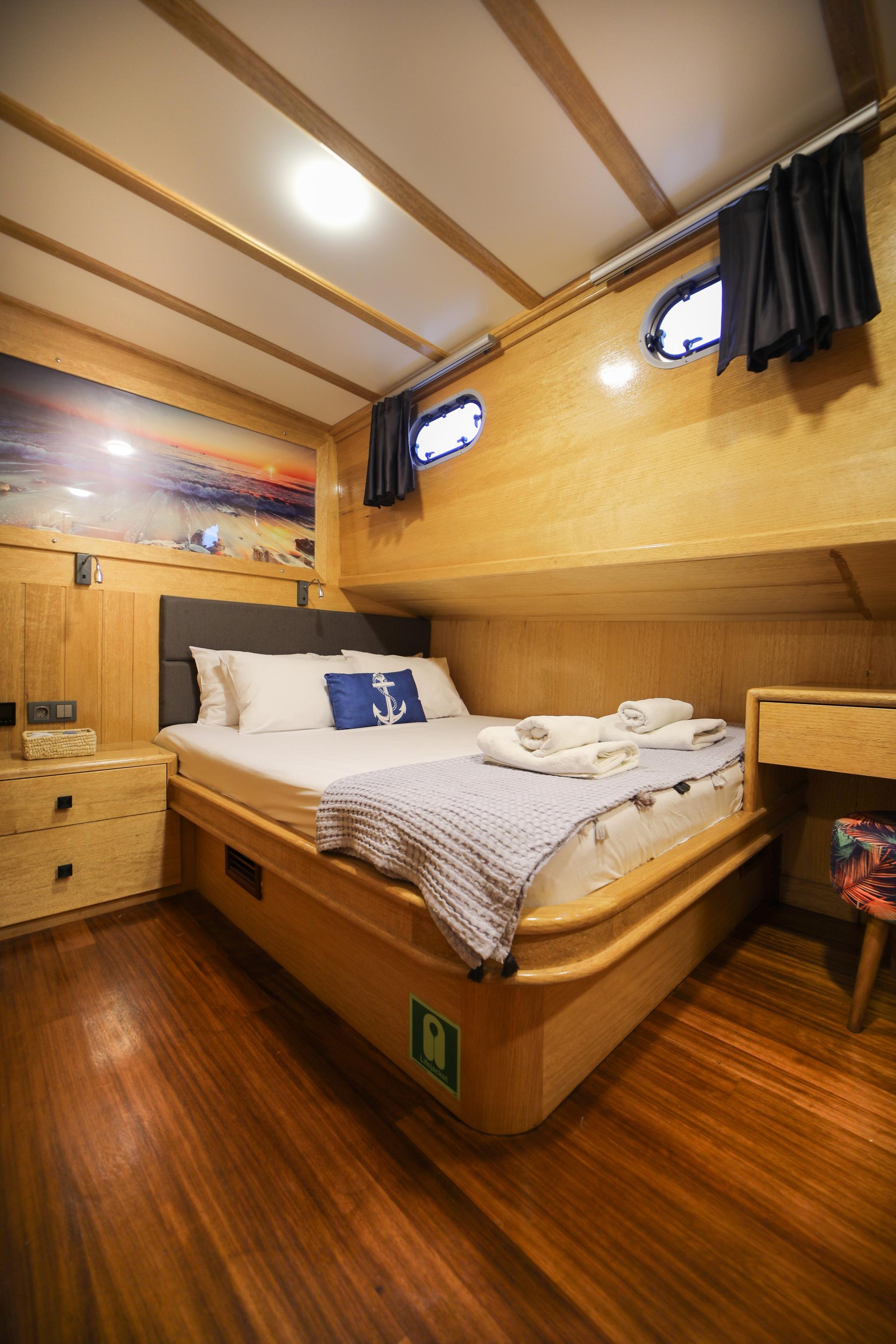 yacht guest cabin with double bed, wooden paneling, two portholes and bedside storage