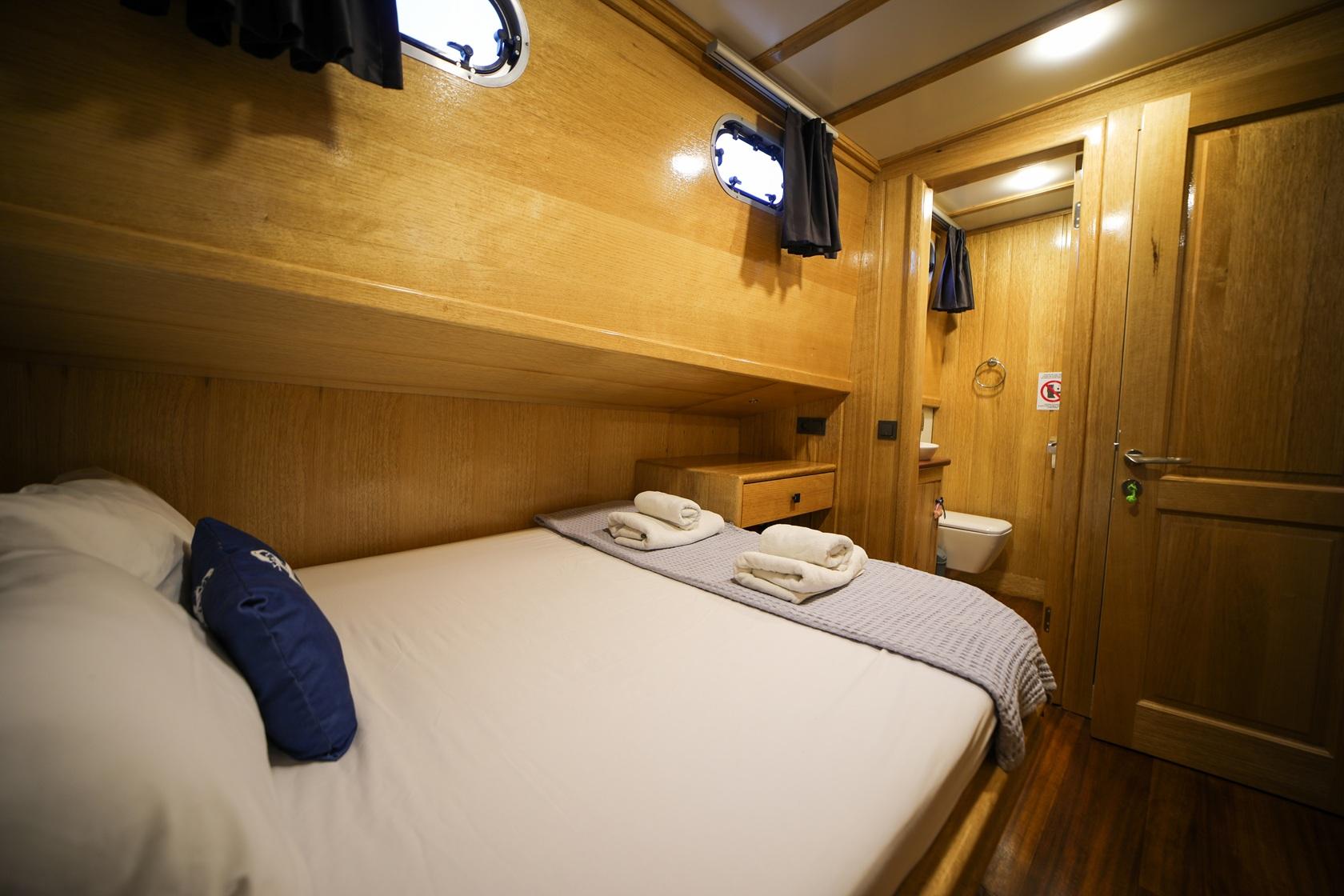 yacht guest cabin featuring double bed with white linens, built-in storage and en-suite bathroom