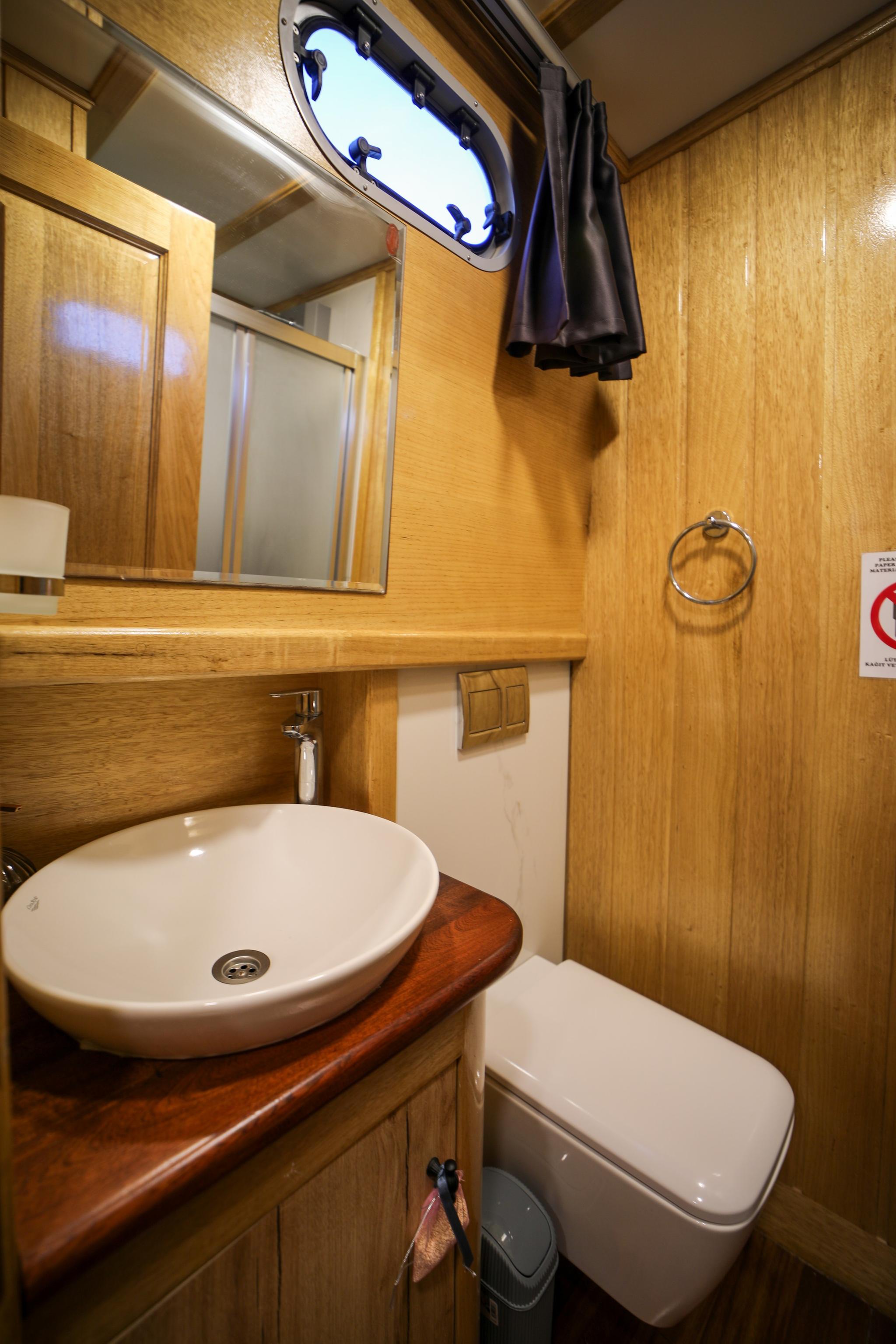 yacht bathroom with white oval sink on wooden countertop and wall-mounted toilet