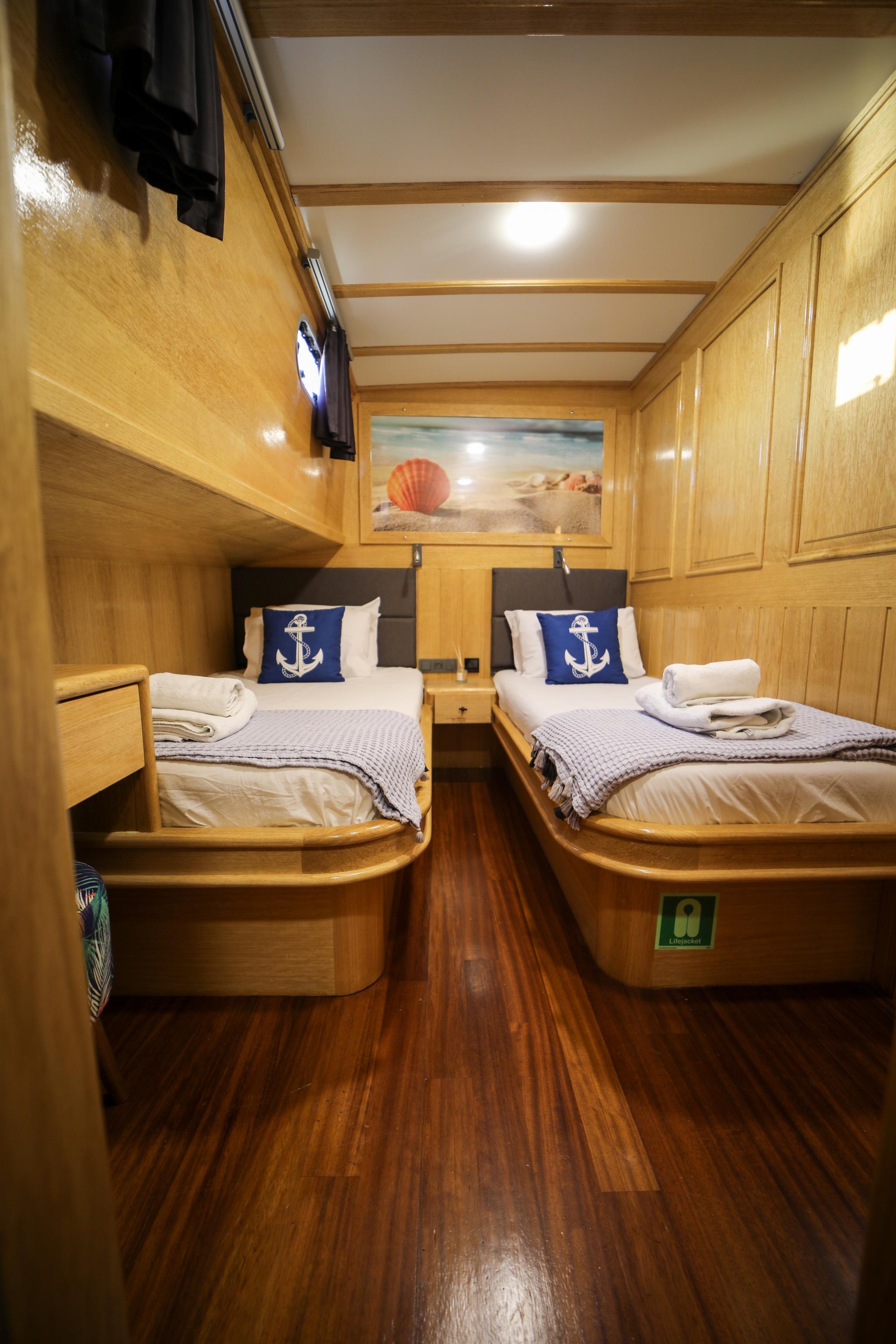 yacht twin cabin with two single beds, anchor pillows, wooden paneling and teak flooring