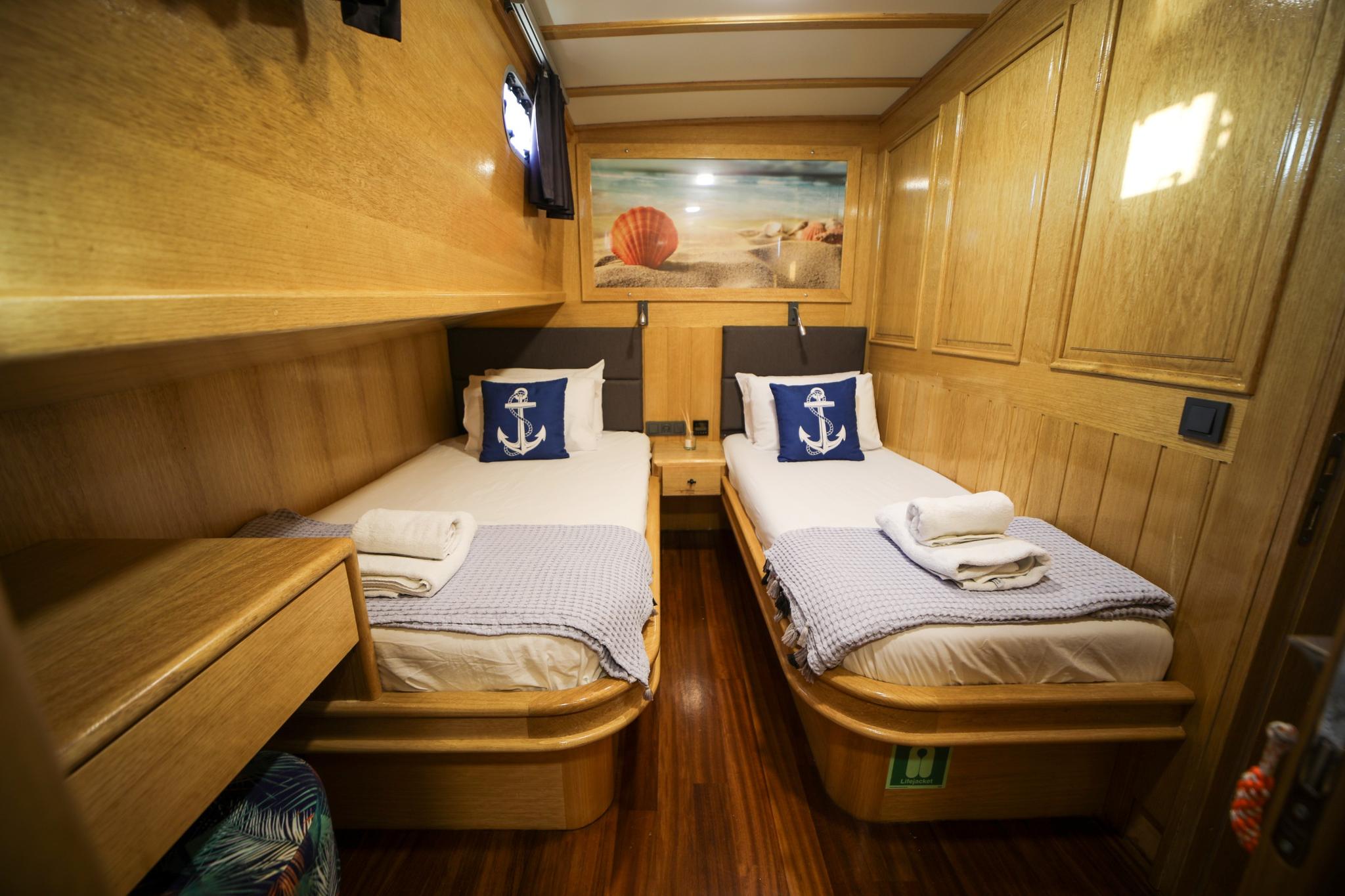 yacht guest cabin with two single beds, nautical anchor pillows, and warm wood paneling