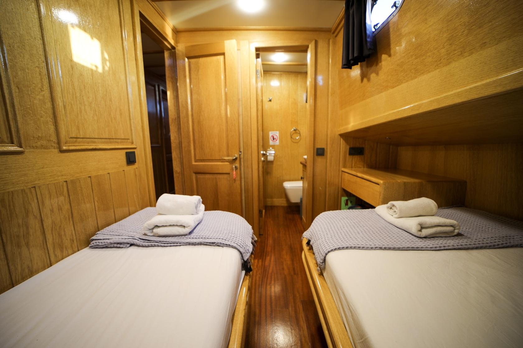 yacht twin cabin featuring two single beds with white linens and private ensuite bathroom