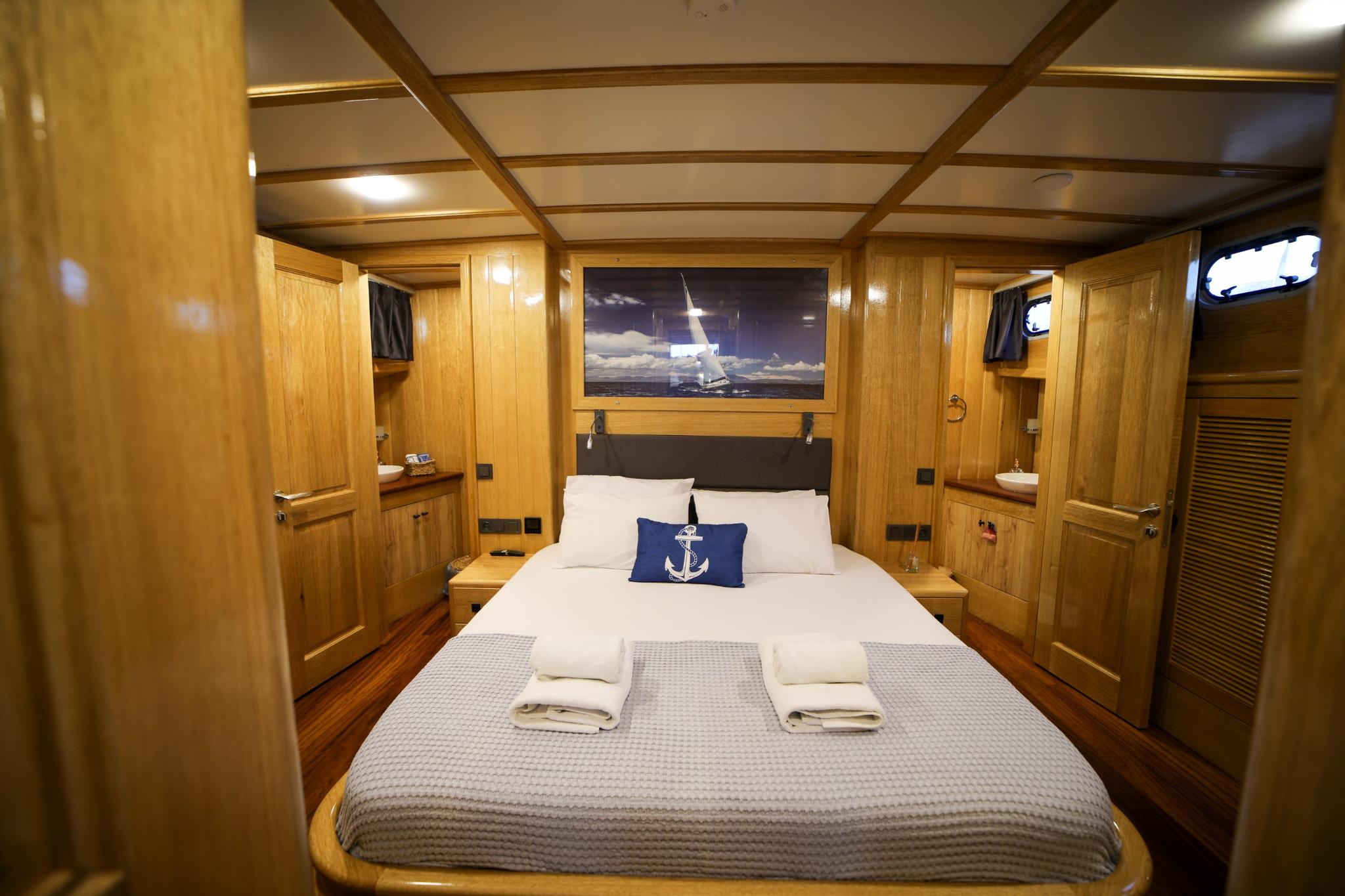 yacht guest cabin with double bed, wooden paneling, nautical artwork and built-in storage