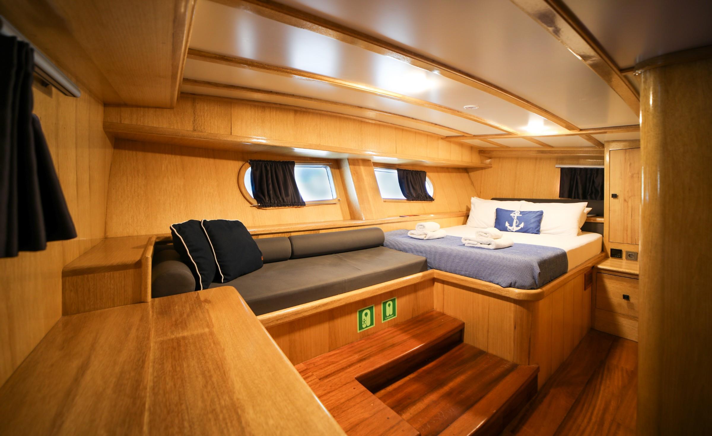 yacht guest cabin interior with double bed, gray cushioned seating, and oval portholes