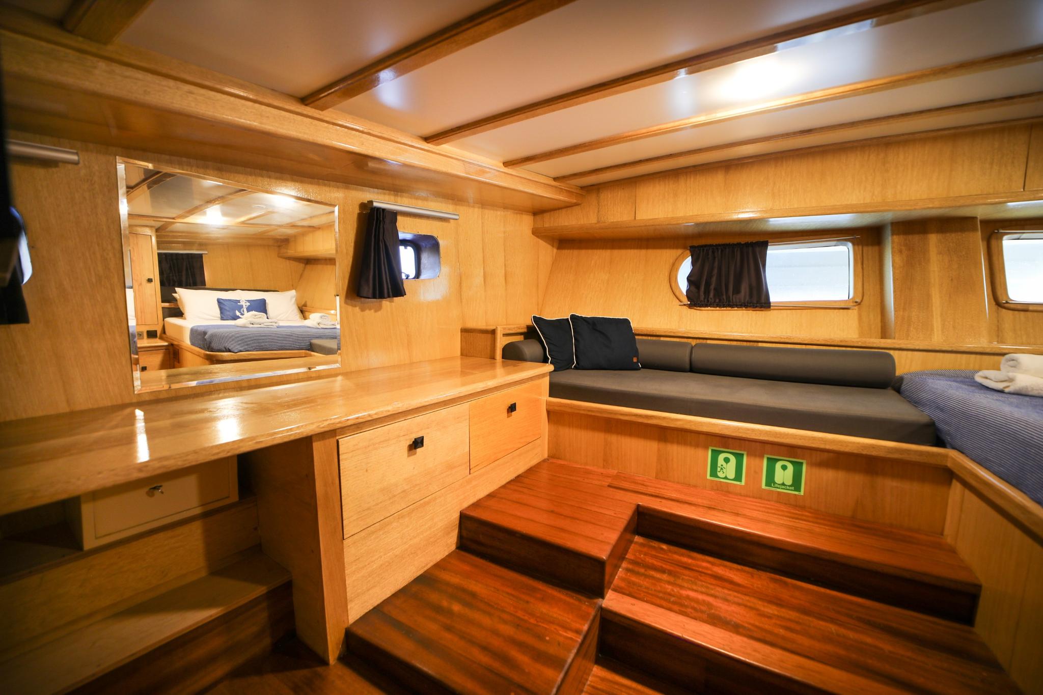 yacht guest cabin featuring single bed with grey bedding, built-in wooden storage drawers, and porthole windows